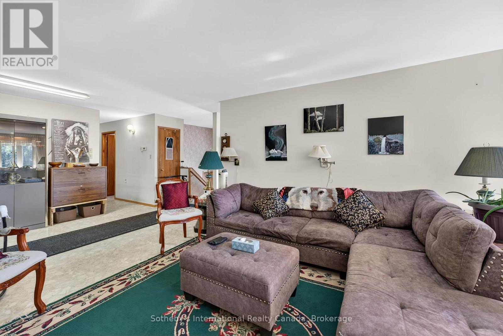 Living room with a purple sectional, matching ottoman, and ornate green rug.