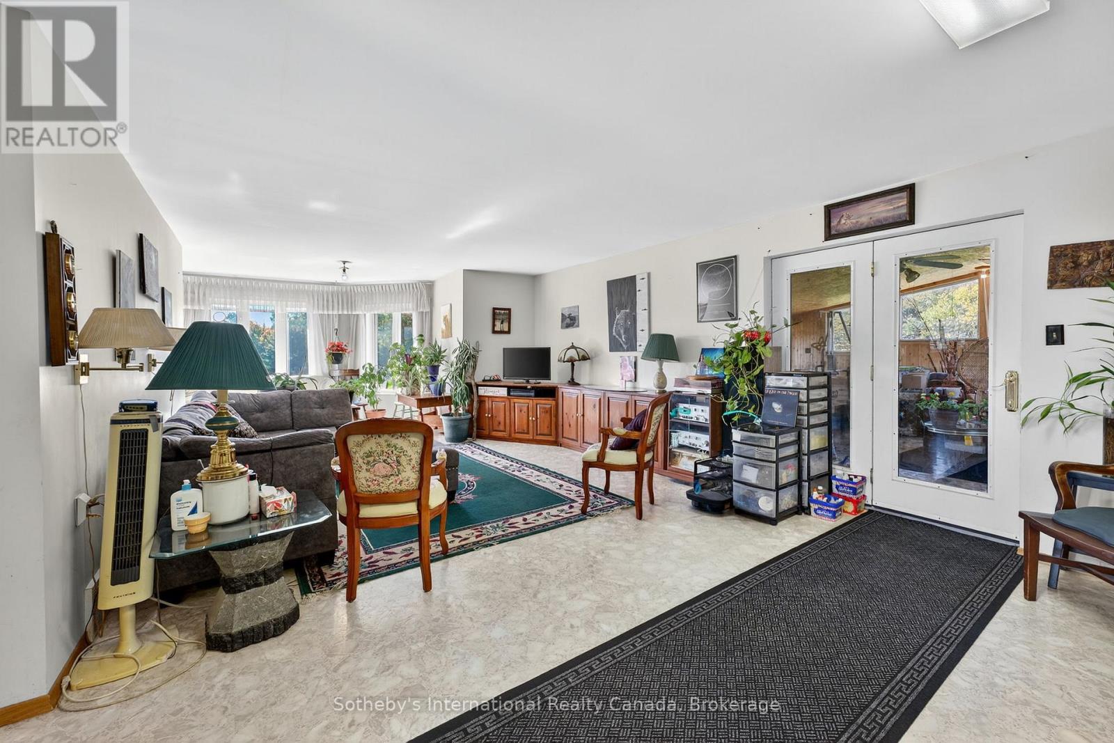 Furnished living room with a gray sofa, wood cabinetry, patterned rugs, and glass doors to a covered outdoor area.