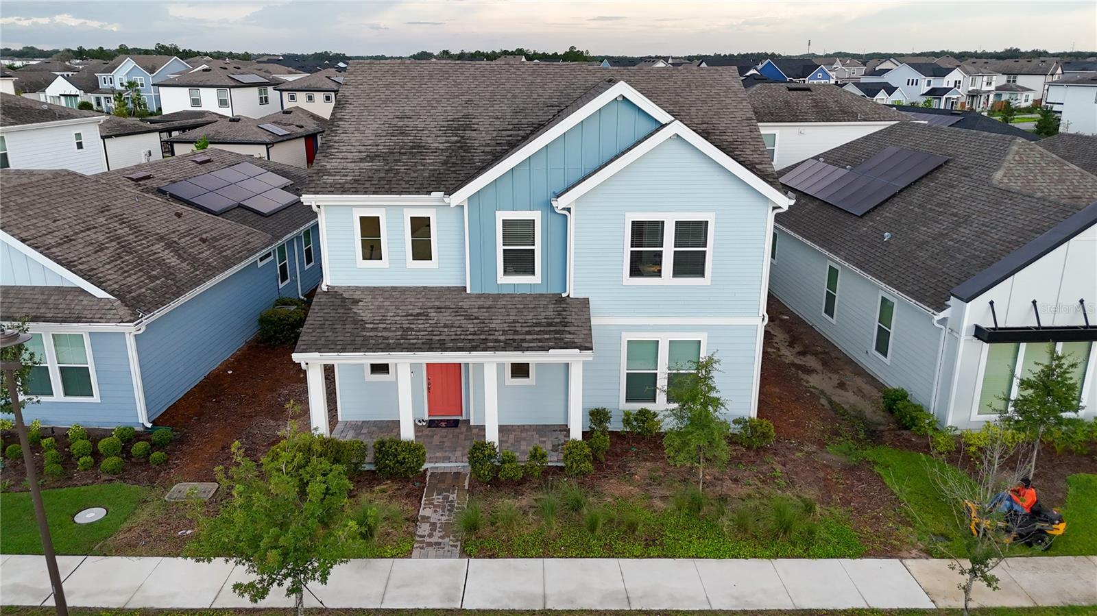 Aerial view of a light-blue two-story home with white trim and a coral-red front door.