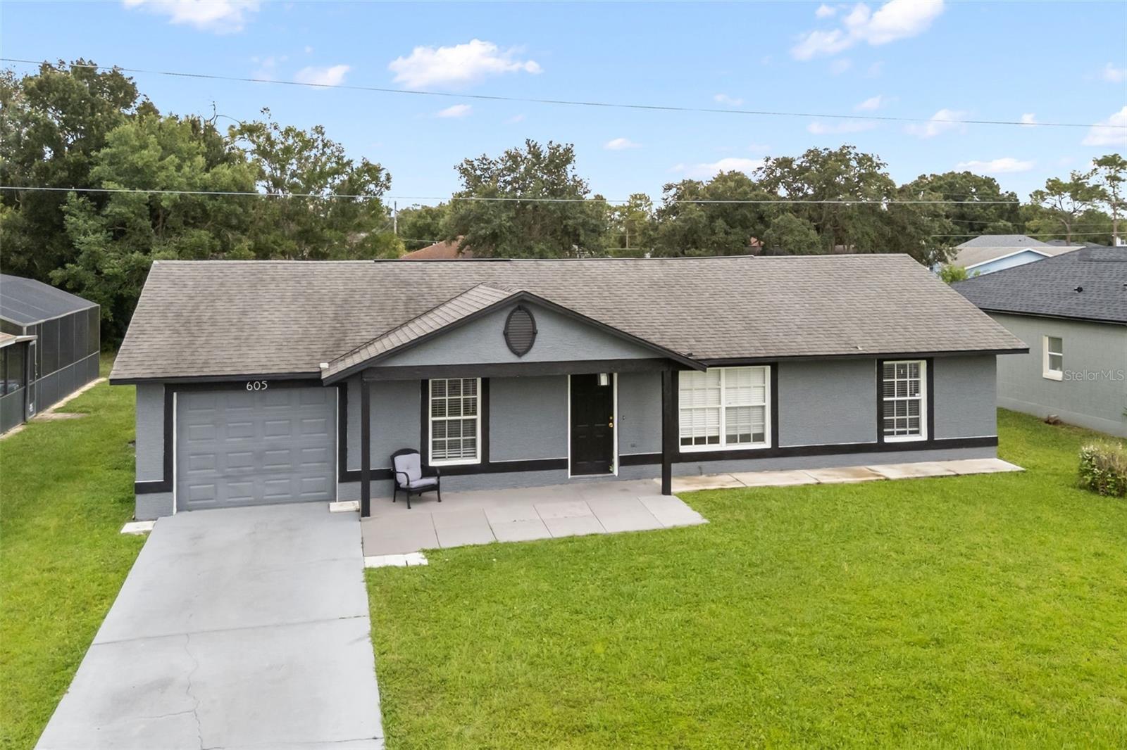 Gray single-story house with attached garage, concrete driveway, and broad green lawn.