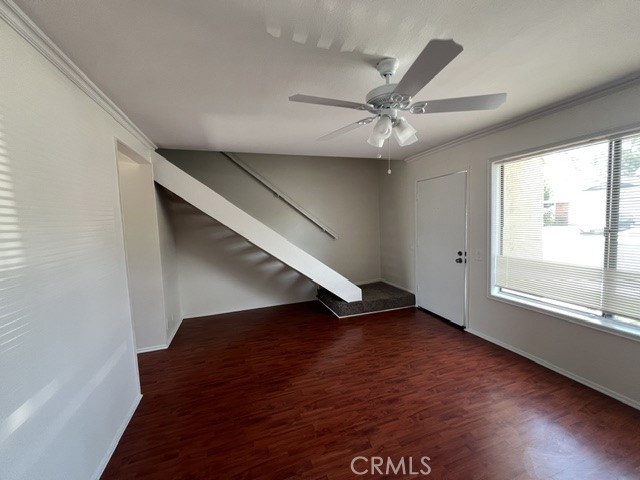 Open room with reddish hardwood floors, a staircase, ceiling fan, and large window.