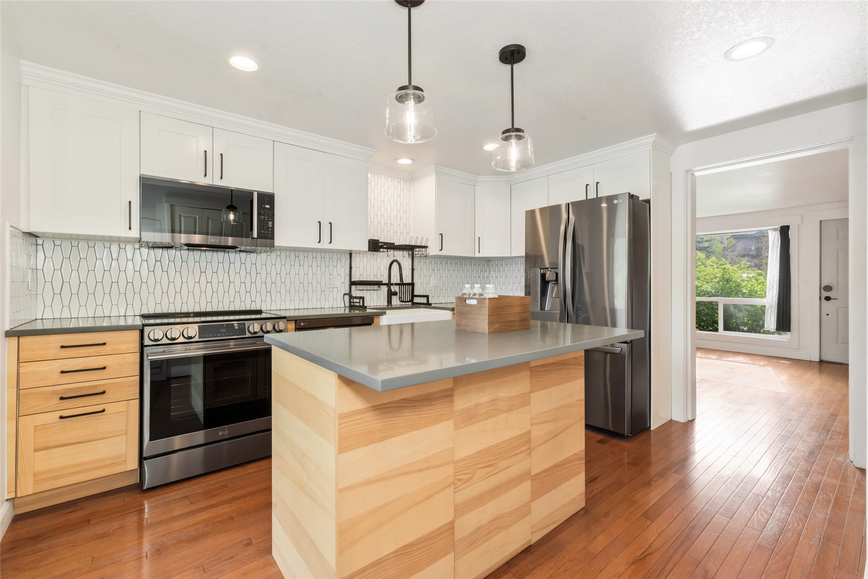Kitchen with a large light-wood island, white cabinetry, geometric tile backsplash, and stainless steel appliances.