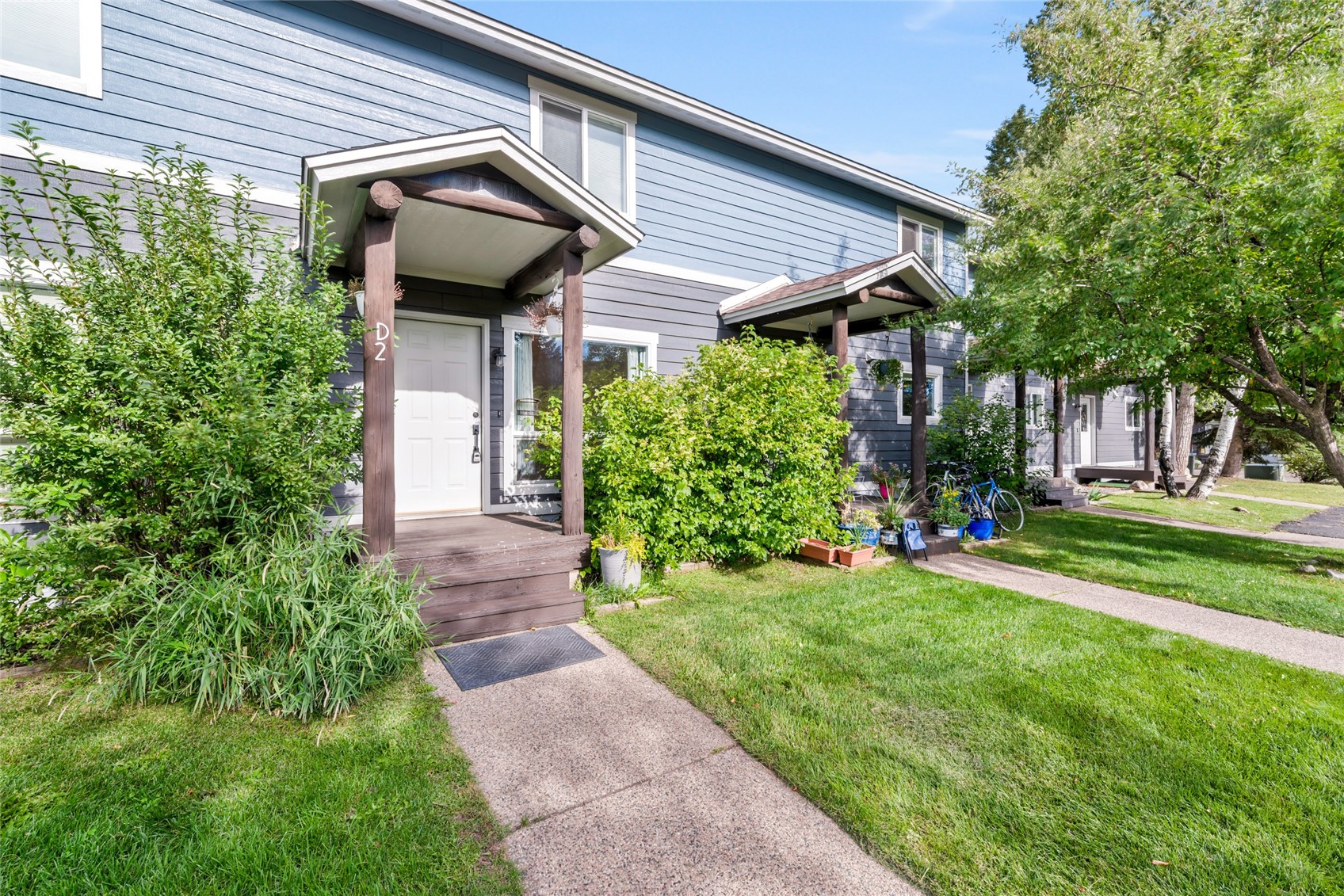 Blue-gray residence entrance marked D2, with a covered porch, shrubs, and a sidewalk.