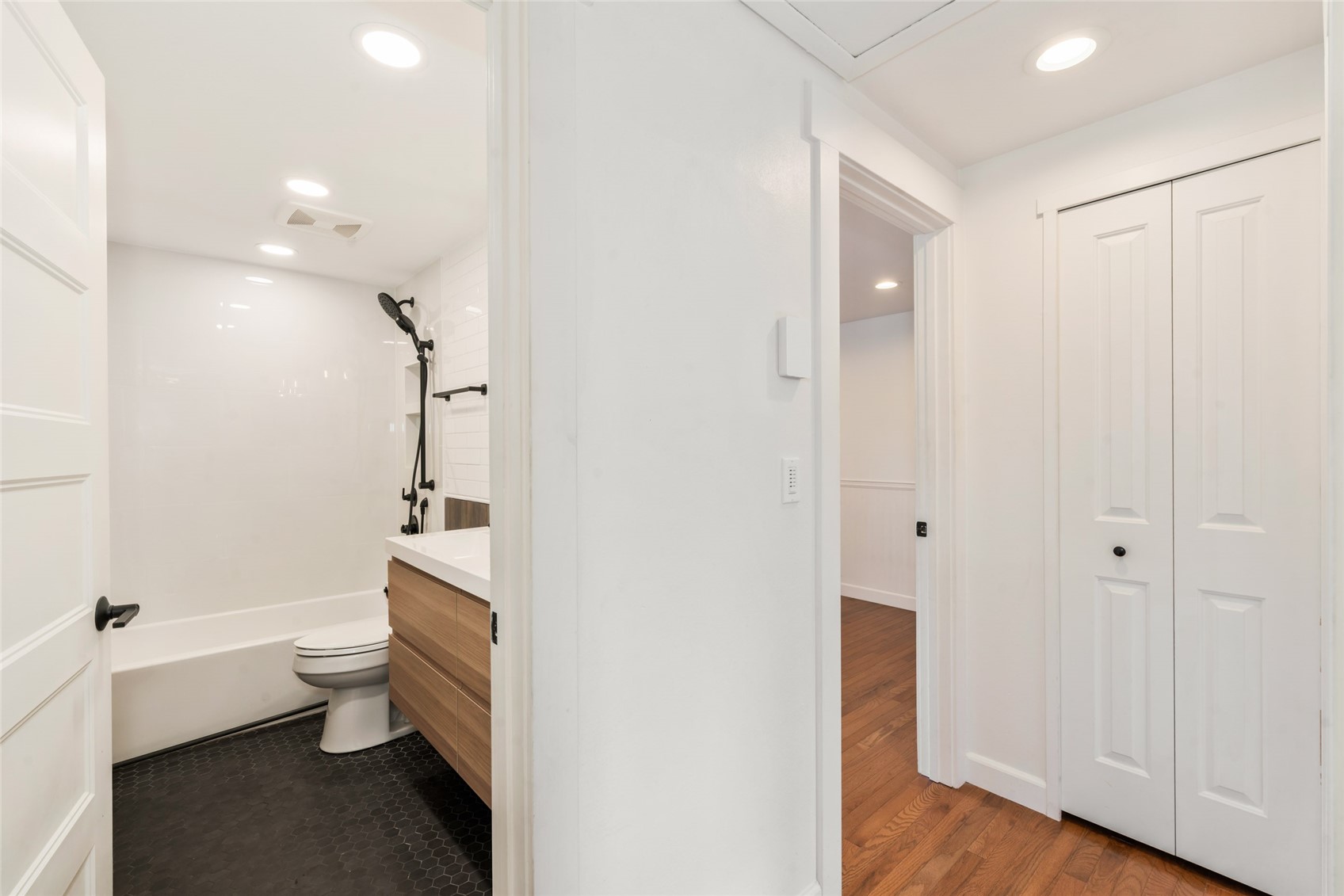 Bathroom with a white tub, black shower fixtures, dark hexagonal tile, and wood-front vanity.