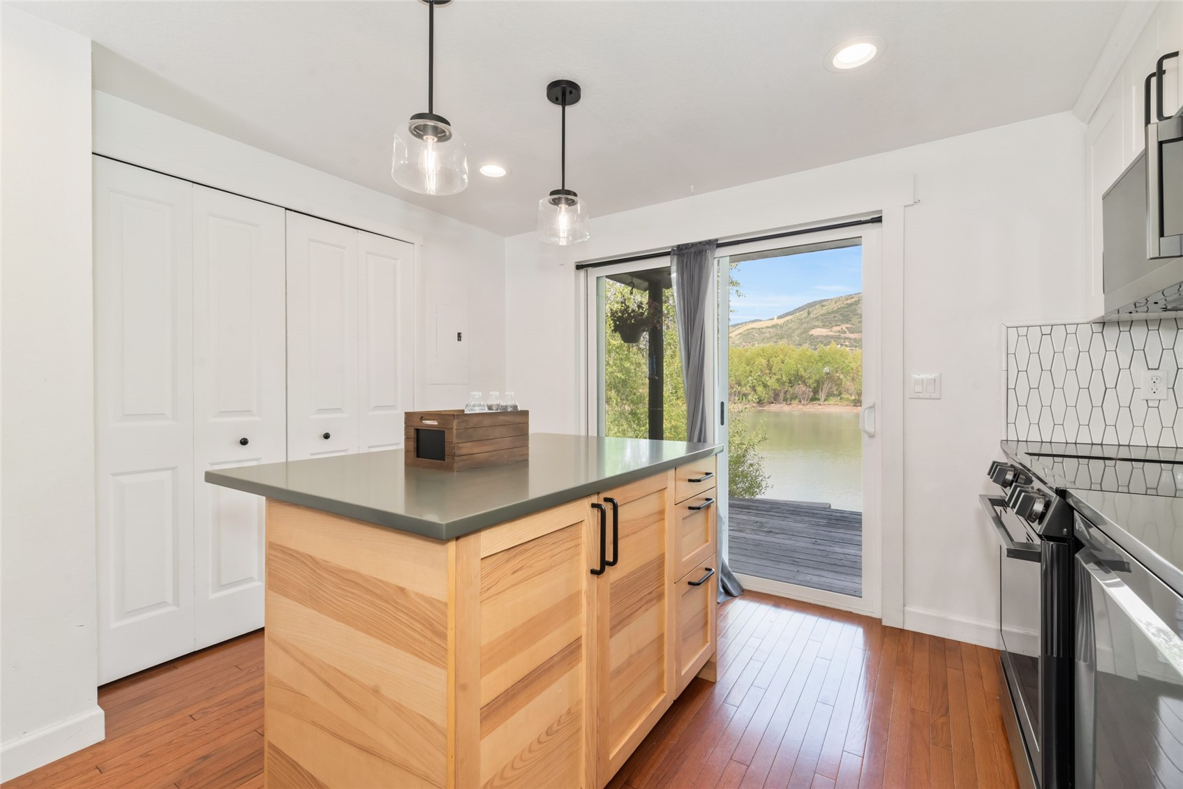 Bright kitchen with a light wood island and sliding doors overlooking water and a hillside.