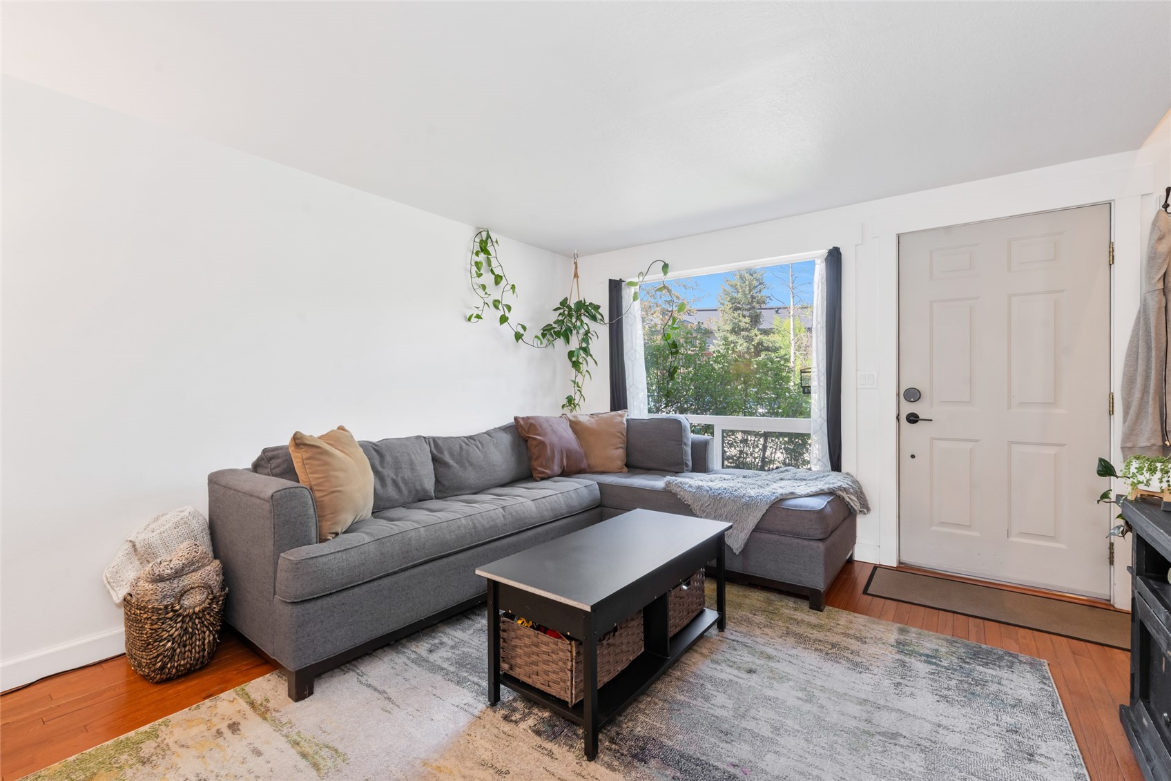Living room with a gray sectional sofa, black coffee table, and a window overlooking trees.