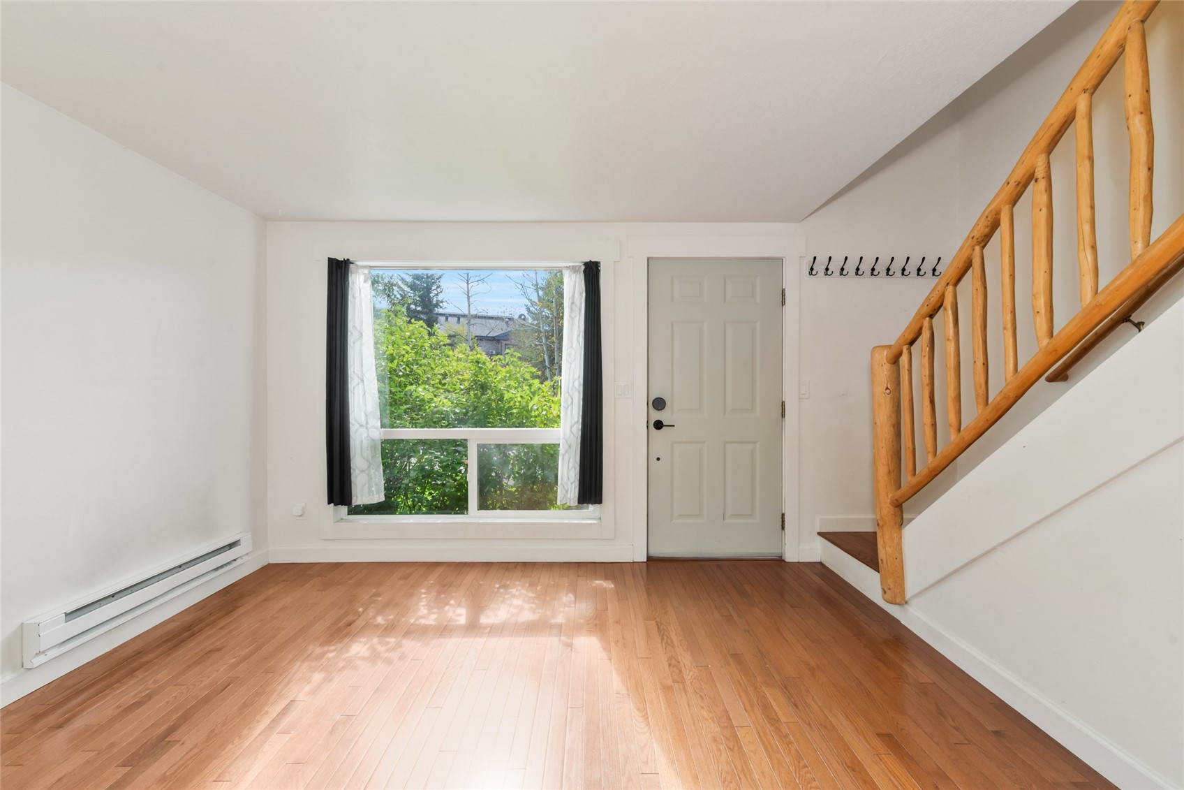Vacant entry area with hardwood floors, a large window, and a wooden staircase.