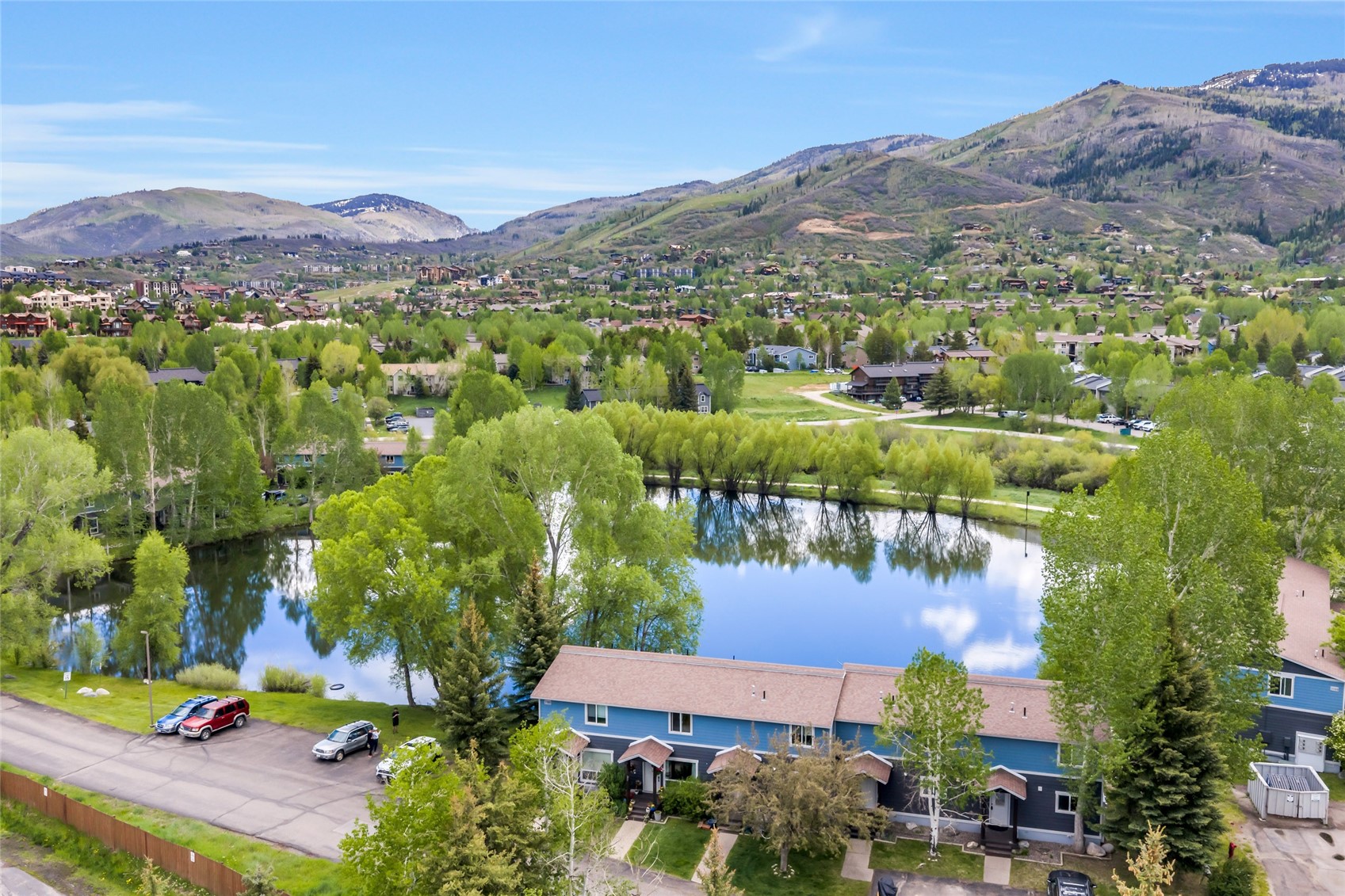 Aerial view of a blue residential building beside a pond, with Steamboat Springs and mountains in the distance.