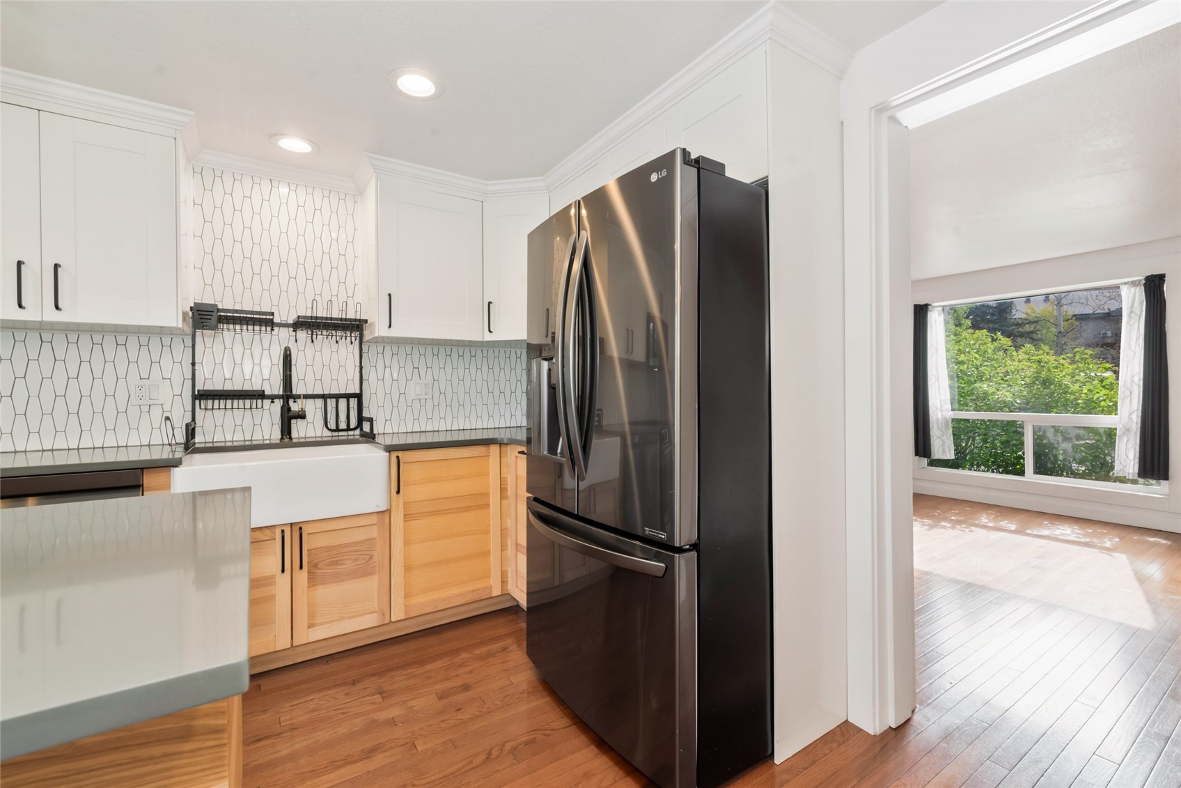 Renovated kitchen with geometric tile backsplash, farmhouse sink, and stainless steel refrigerator.