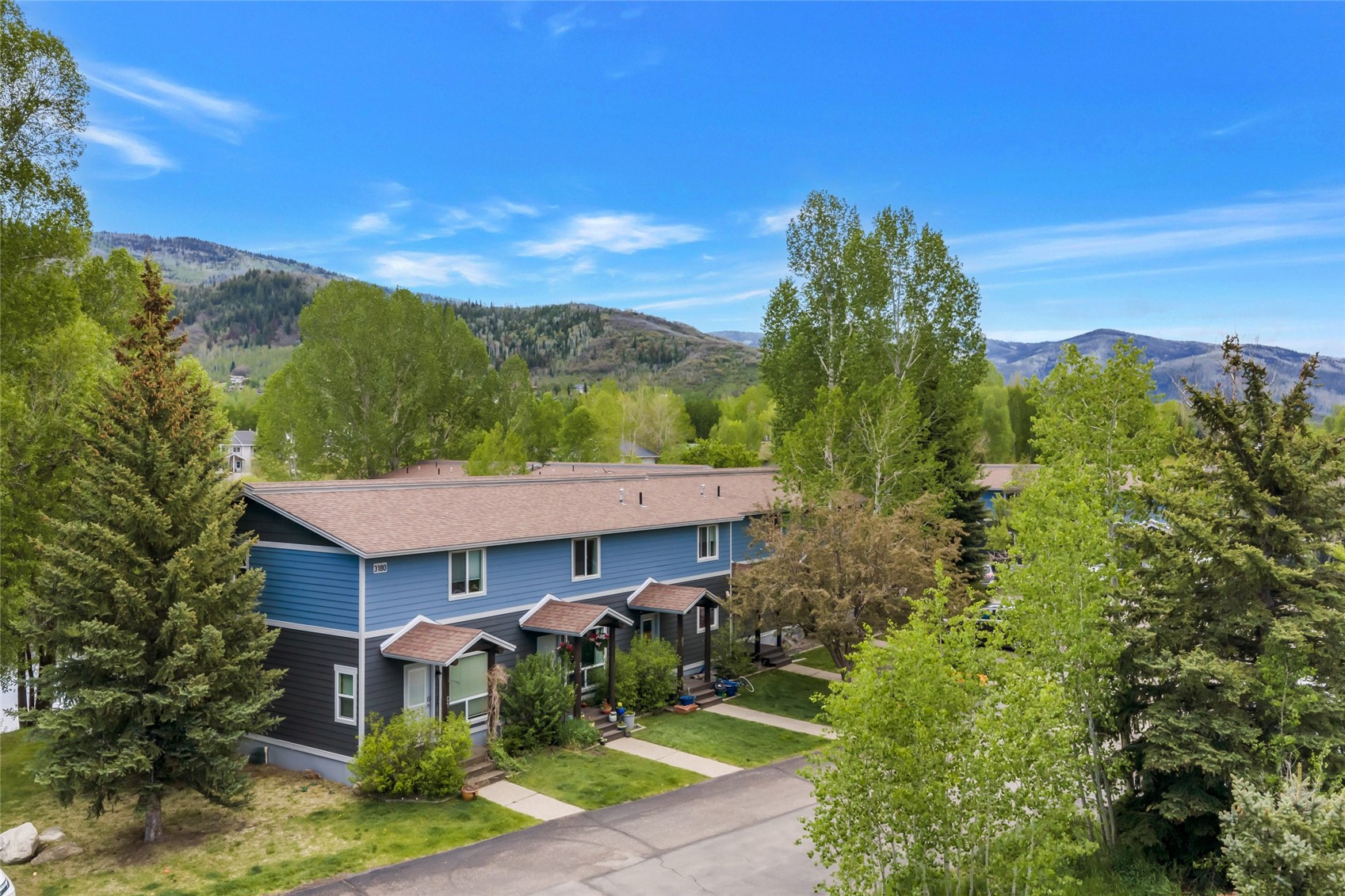 Blue two-story residence among trees, with mountain views behind it.