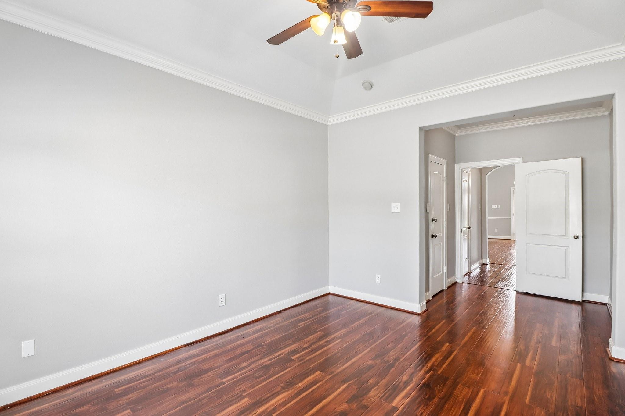 Empty room with dark hardwood floors, gray walls, a ceiling fan, and an open doorway to the hall.