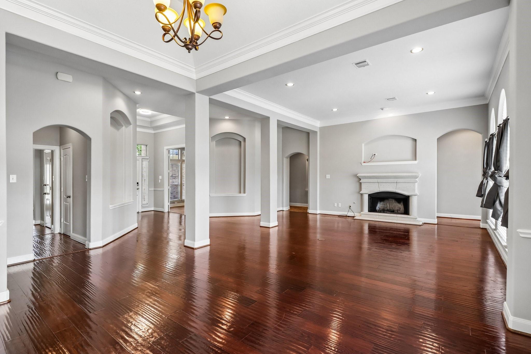 Empty living room with glossy hardwood floors, arched openings, and a white fireplace.