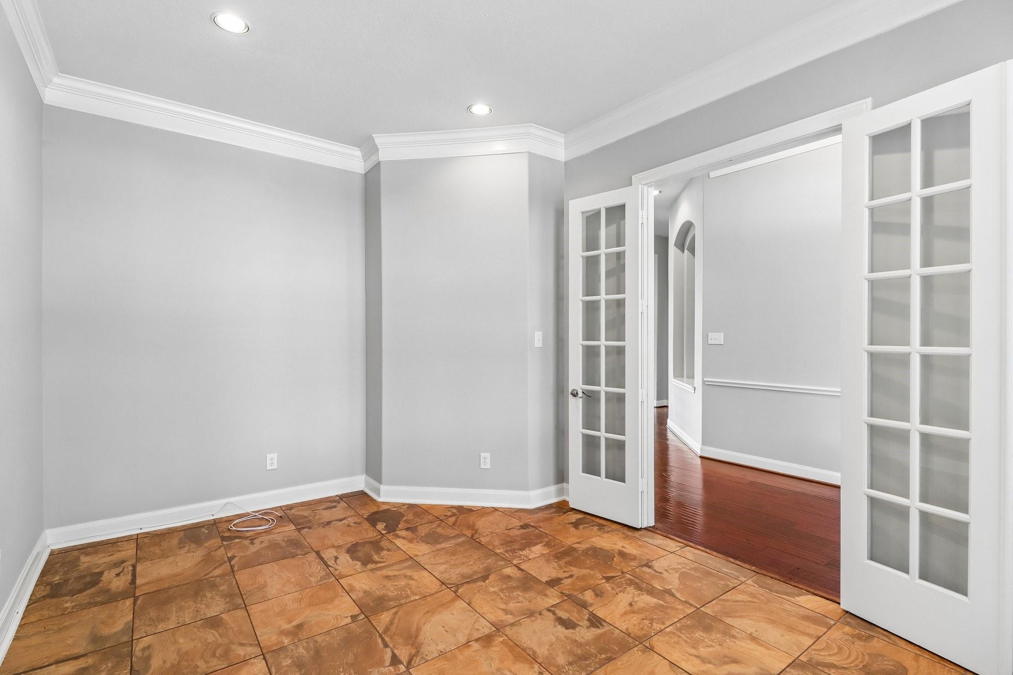 Empty tiled room with gray walls and open French doors to a hardwood-floored room.