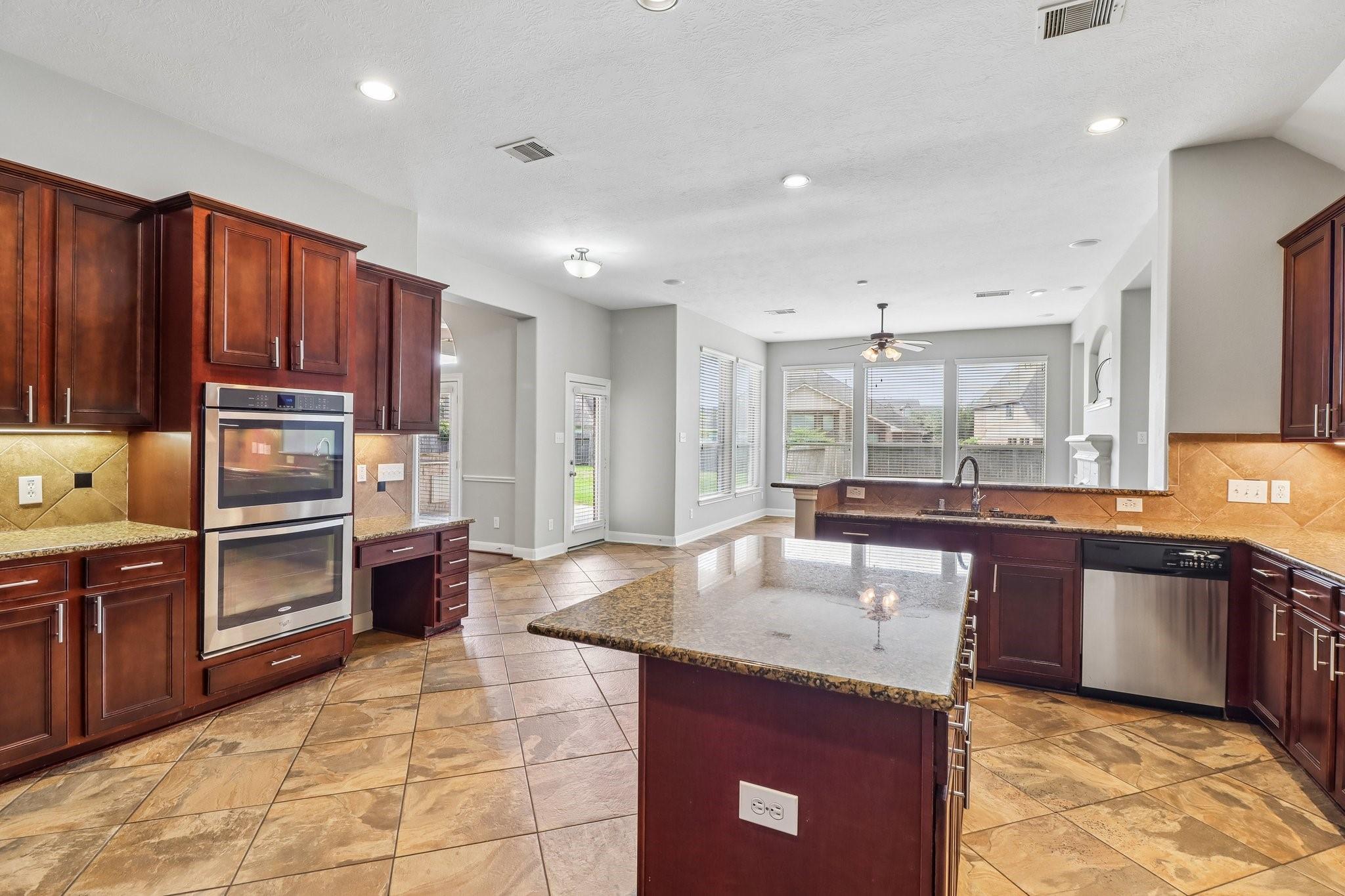 Kitchen with a large granite island, dark cherry cabinets, and double wall ovens.