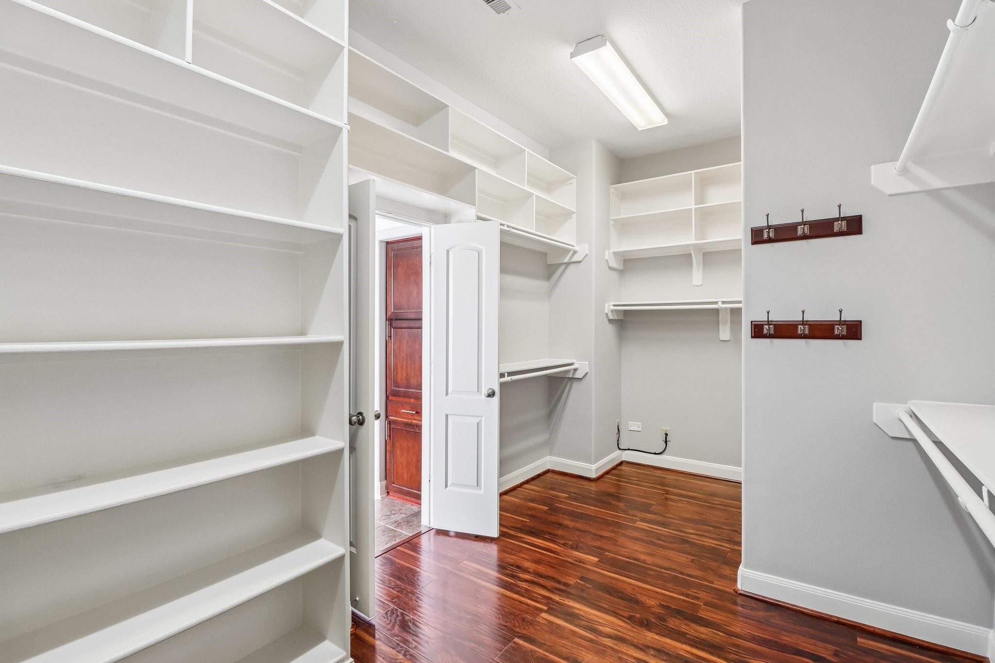 Walk-in closet with extensive white shelving, wall hooks, and polished hardwood floors.