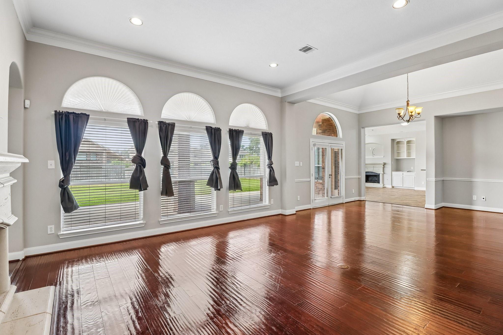 Empty living room with glossy hardwood floors and three curtained windows topped by fanlights.