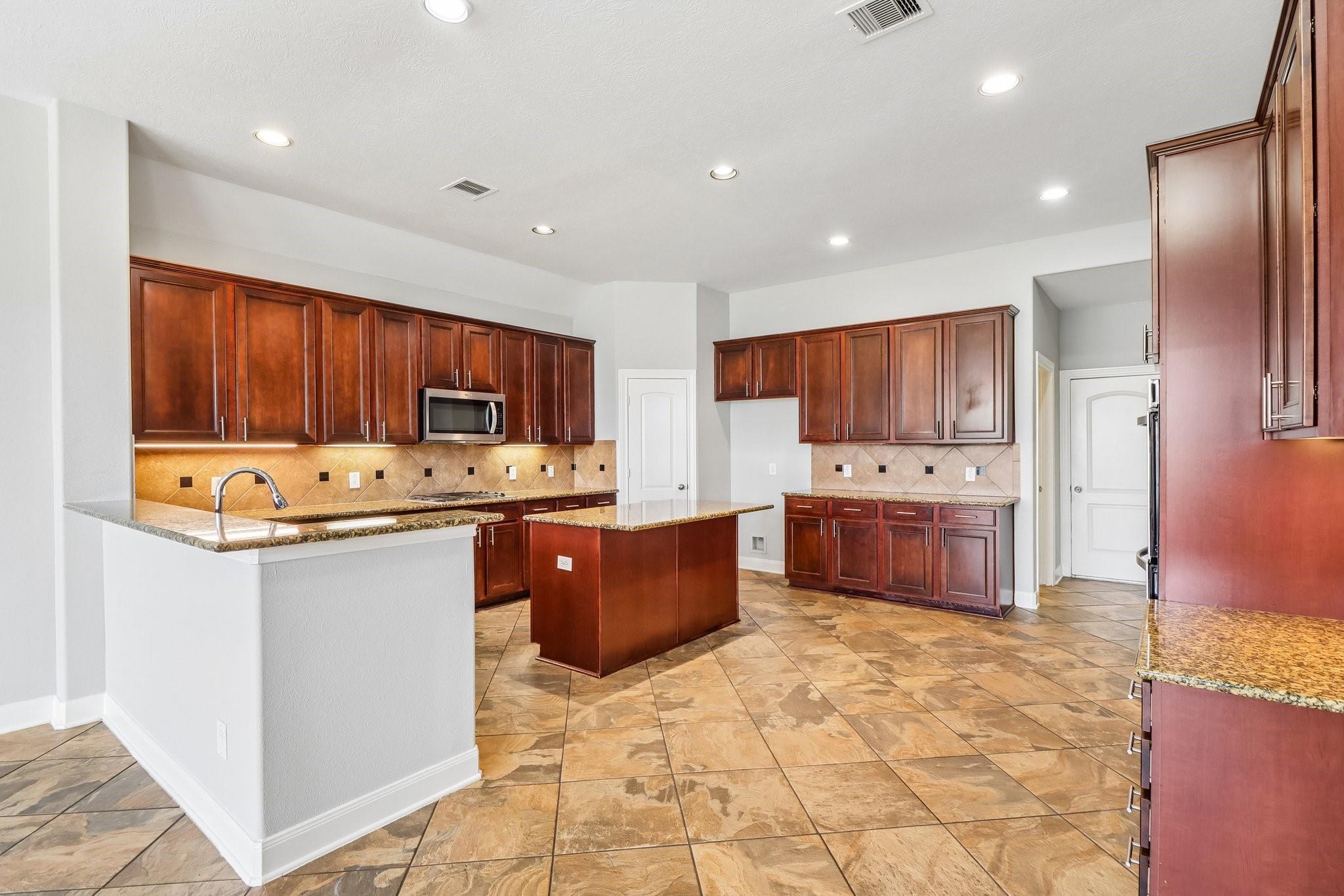 Spacious kitchen with dark wood cabinets, granite counters, a central island, and patterned tile floors.