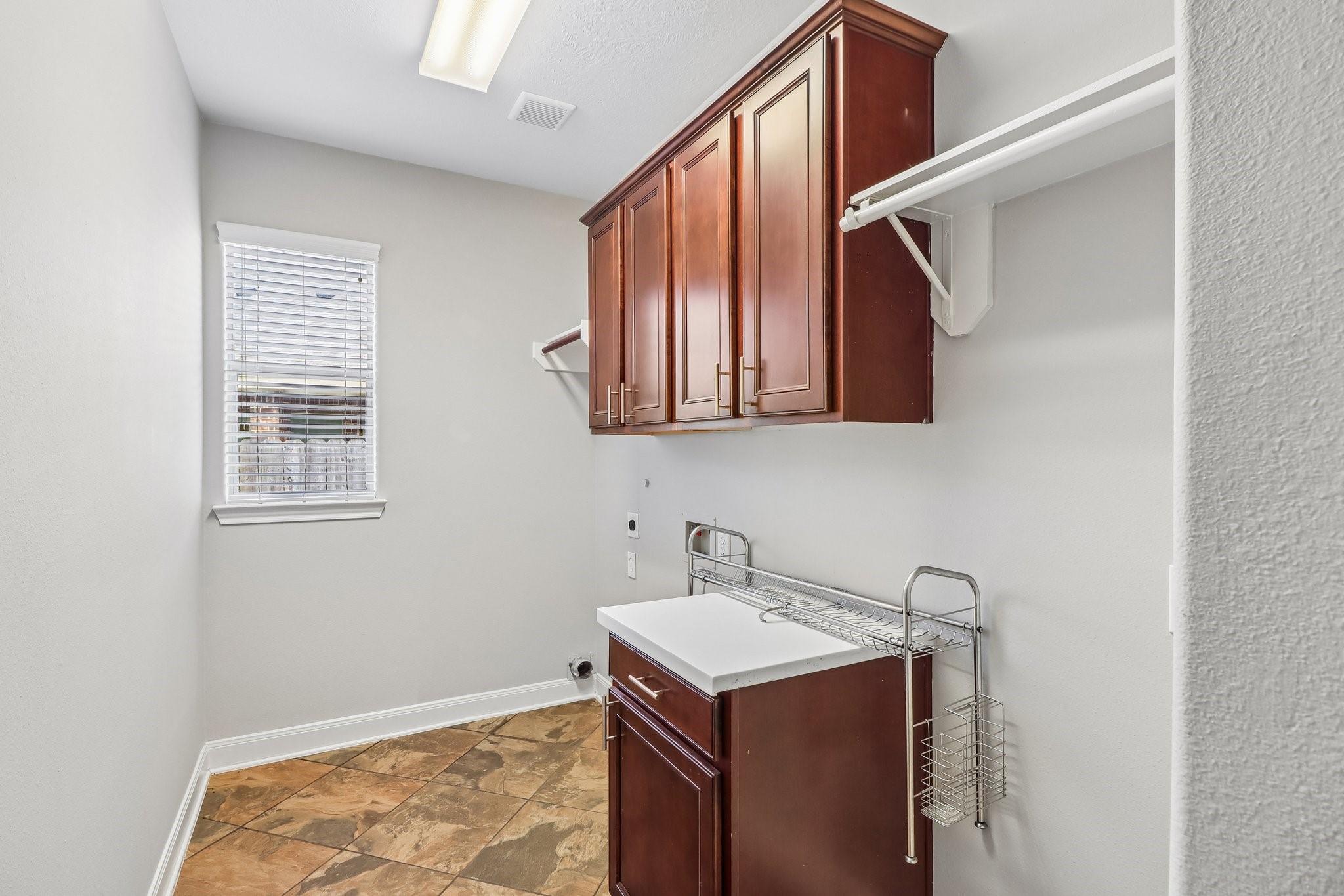 Laundry room with cherry cabinets, a white counter, drying racks, and patterned tile floor.