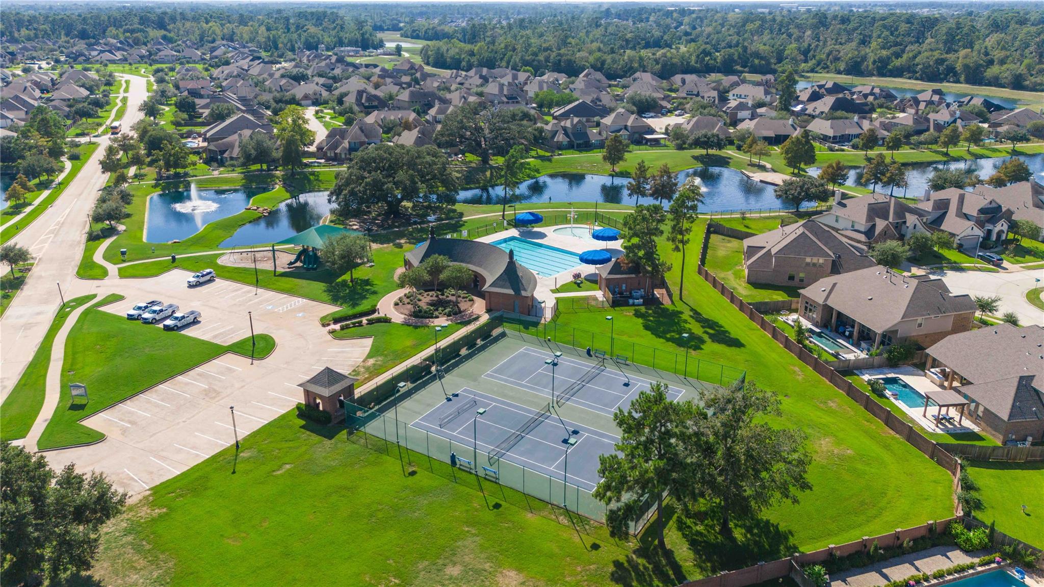 Aerial view of neighborhood amenities with a pool, tennis courts, and a fountain pond.