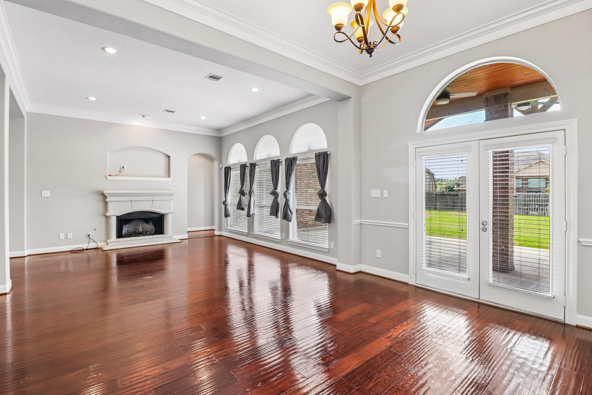 Empty living room with glossy hardwood floors, a white fireplace, and glass patio doors.
