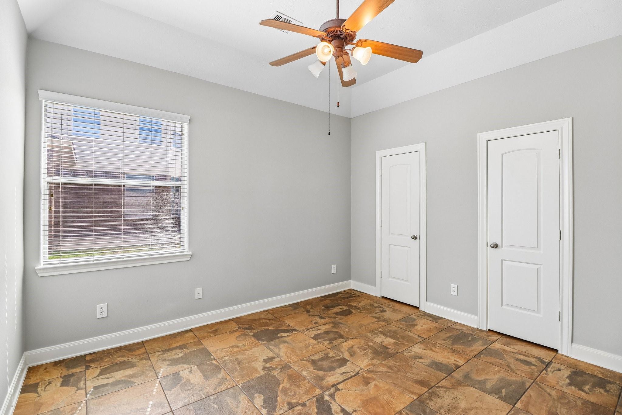Empty room with patterned brown tile flooring, a large window, two doors, and a ceiling fan.