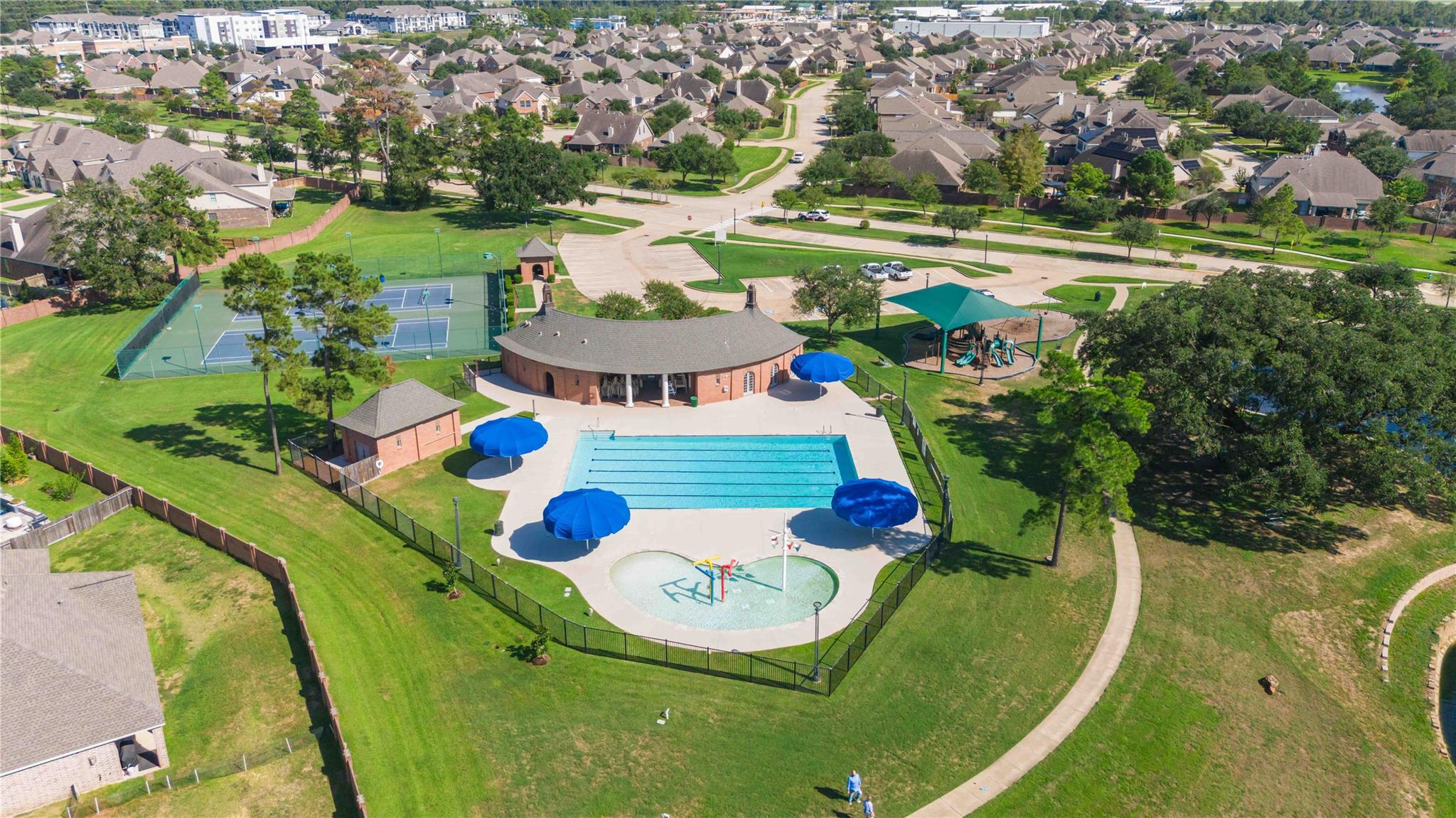 Aerial view of a neighborhood pool, splash pad, tennis courts, playground, and clubhouse.