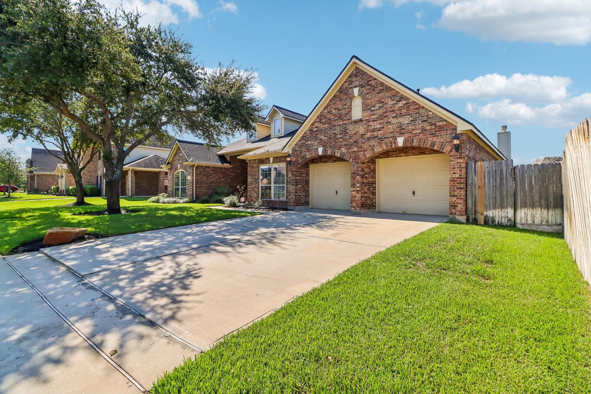 Brick house with two garage doors, a wide driveway, and a mature shade tree.