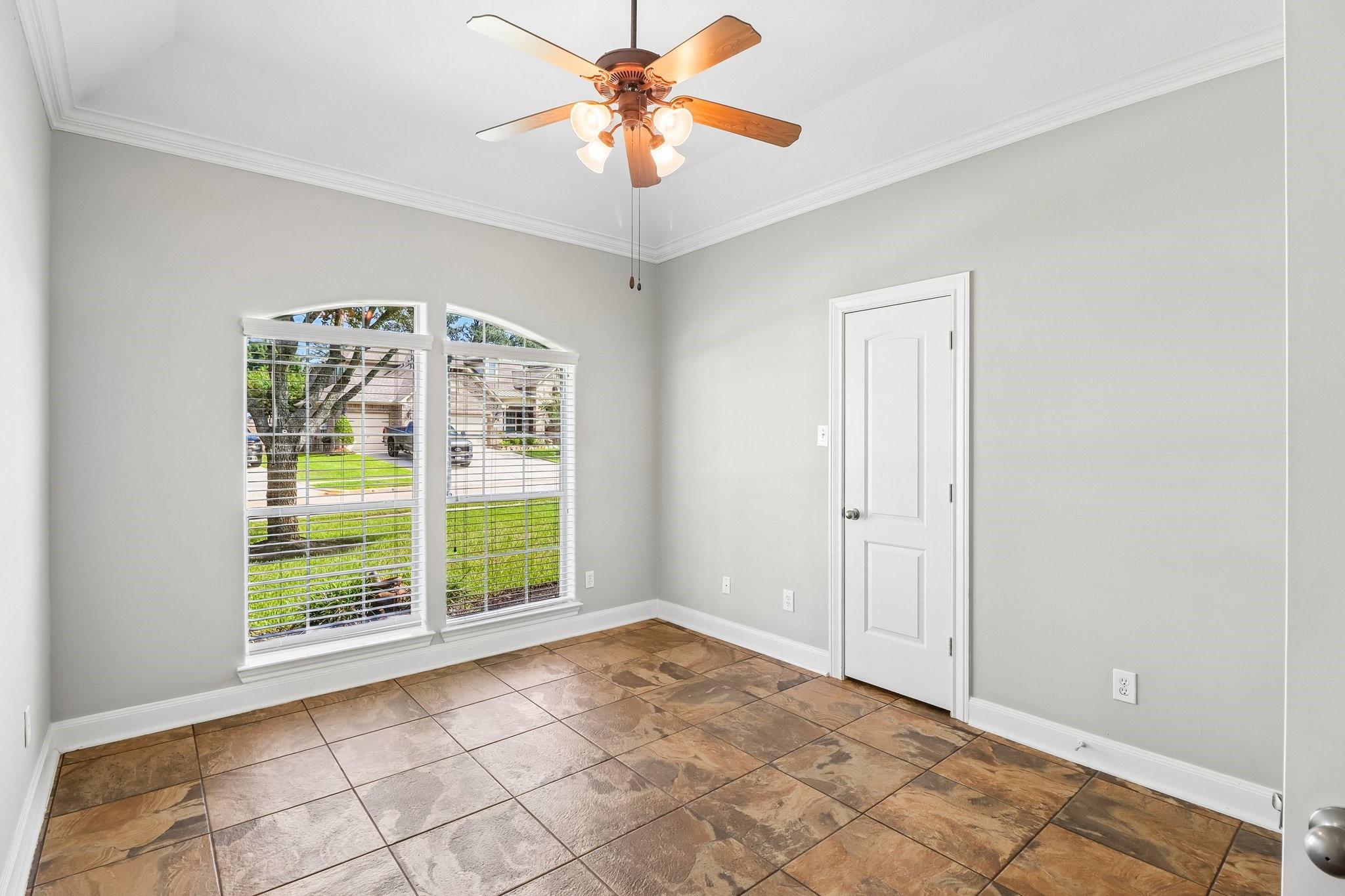 Vacant room with brown tile floors, two blinded windows, and a ceiling fan.