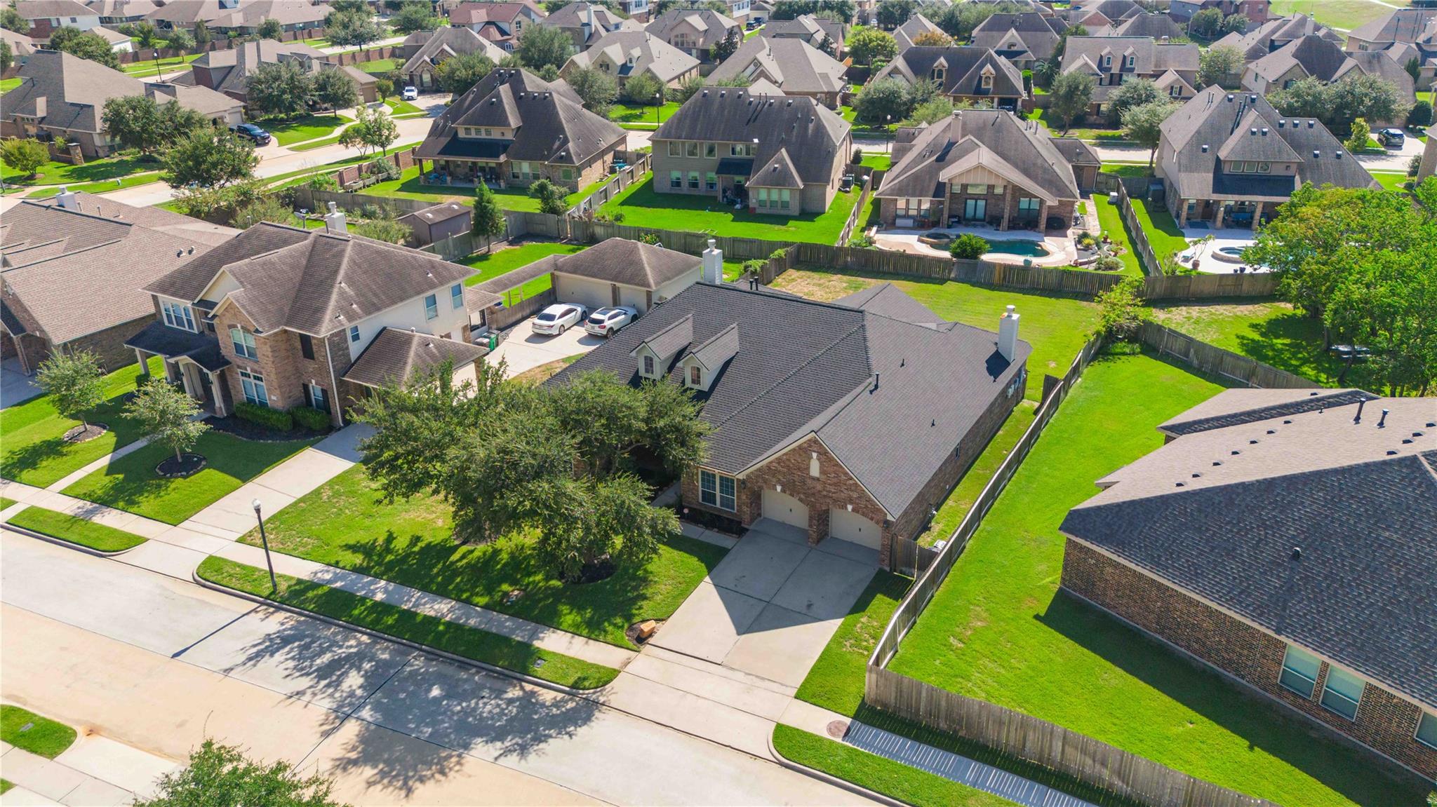 Aerial view of a suburban neighborhood with detached homes, green lawns, and a backyard pool.