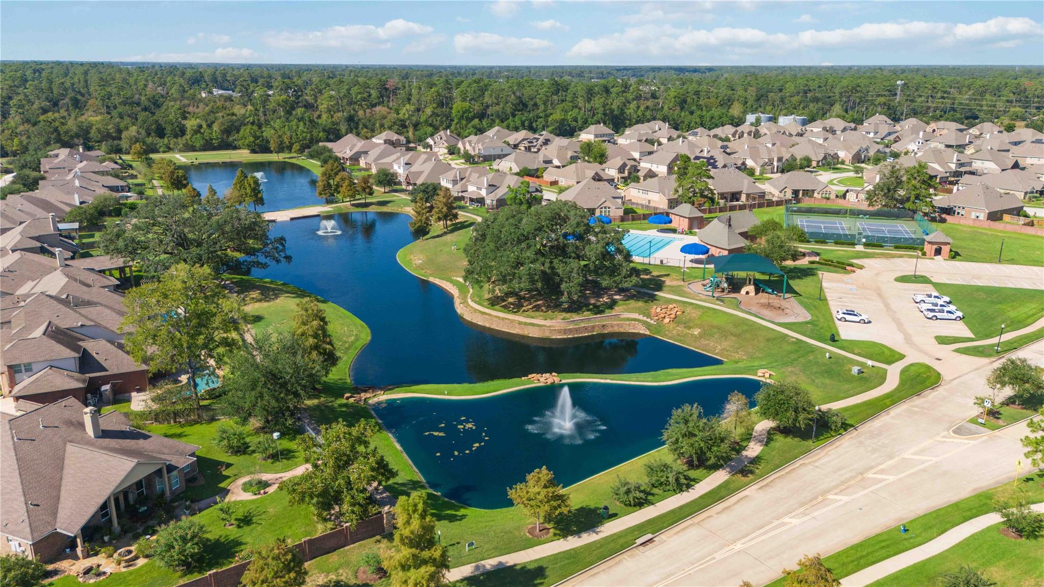 Aerial view of homes around landscaped ponds, with a pool, tennis courts, and playground.