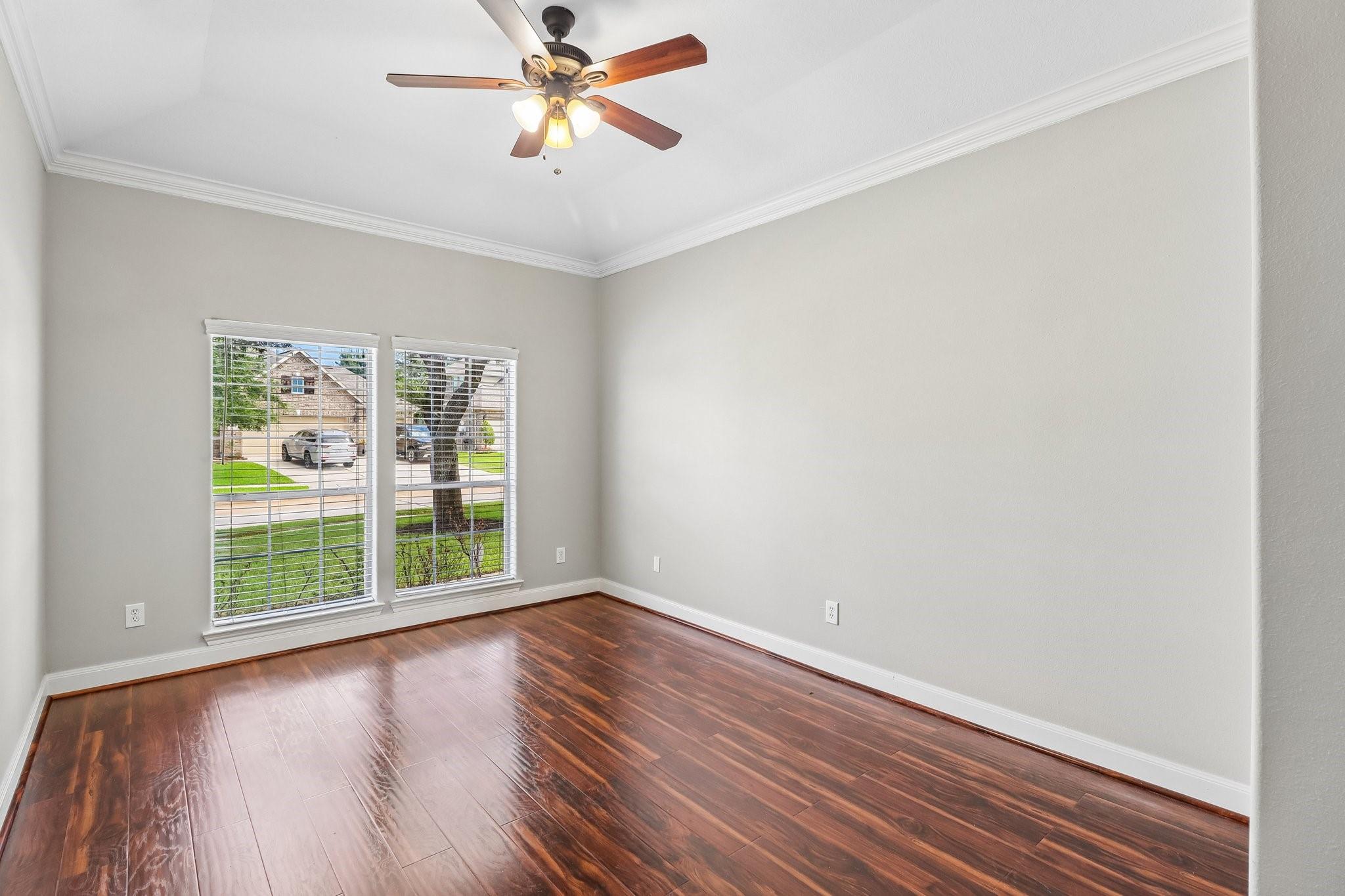 Vacant room with dark wood floors, two blind-covered windows, and a ceiling fan.