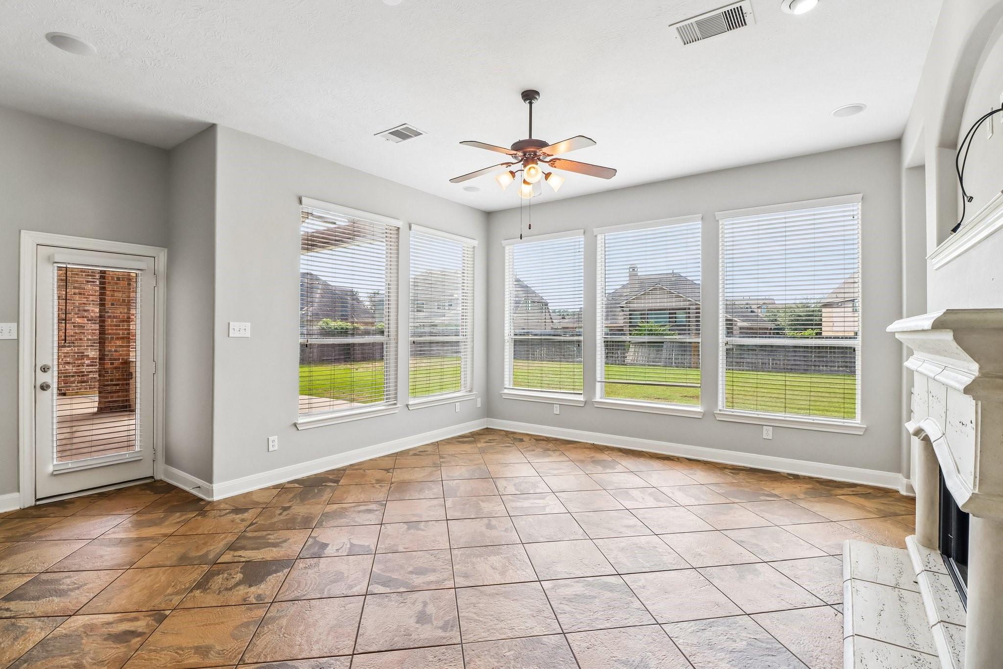 Bright empty room with tiled floors, five large windows, a ceiling fan, and a white fireplace.