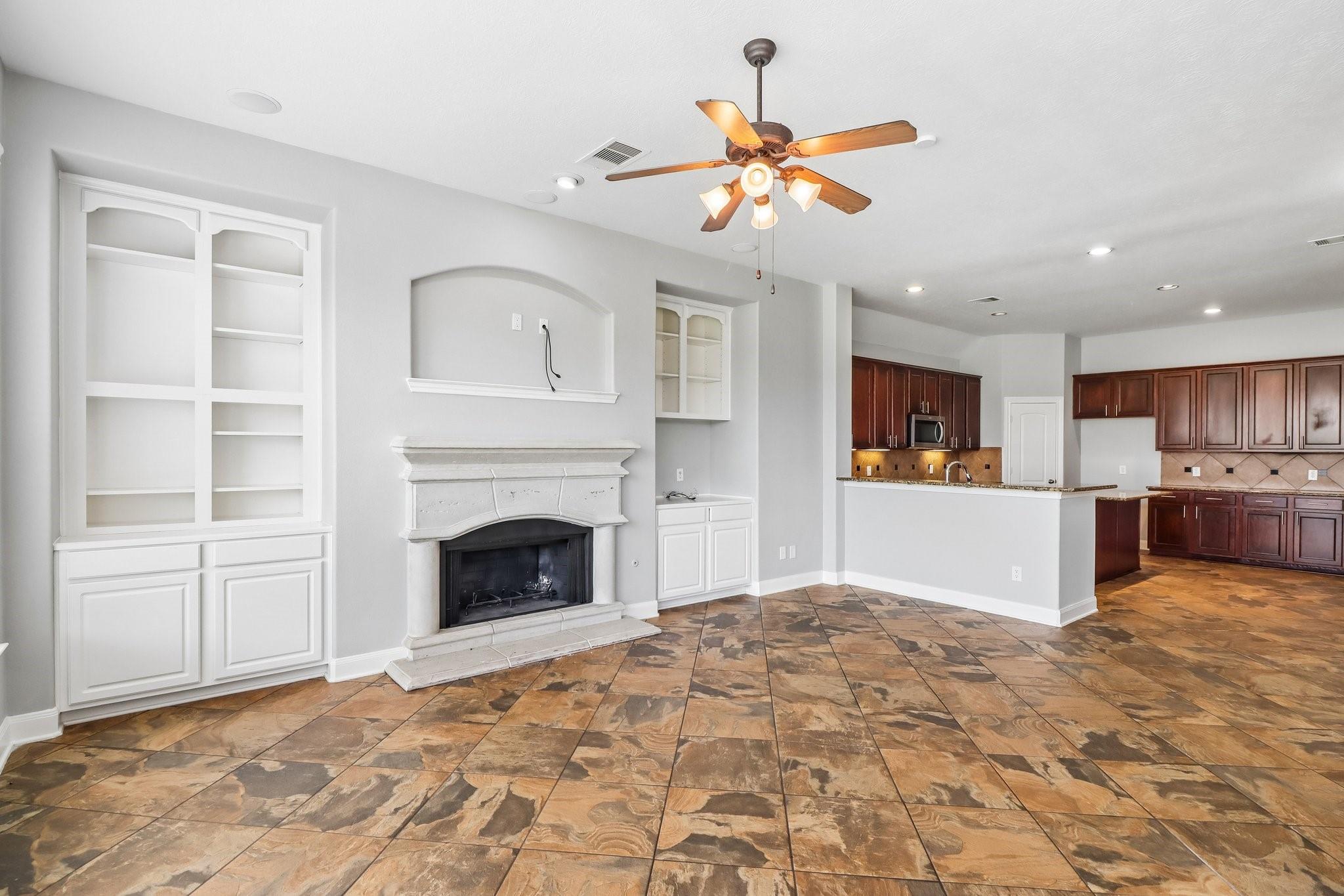 Unfurnished living room with a white fireplace, built-in shelving, patterned tile floor, and open kitchen.