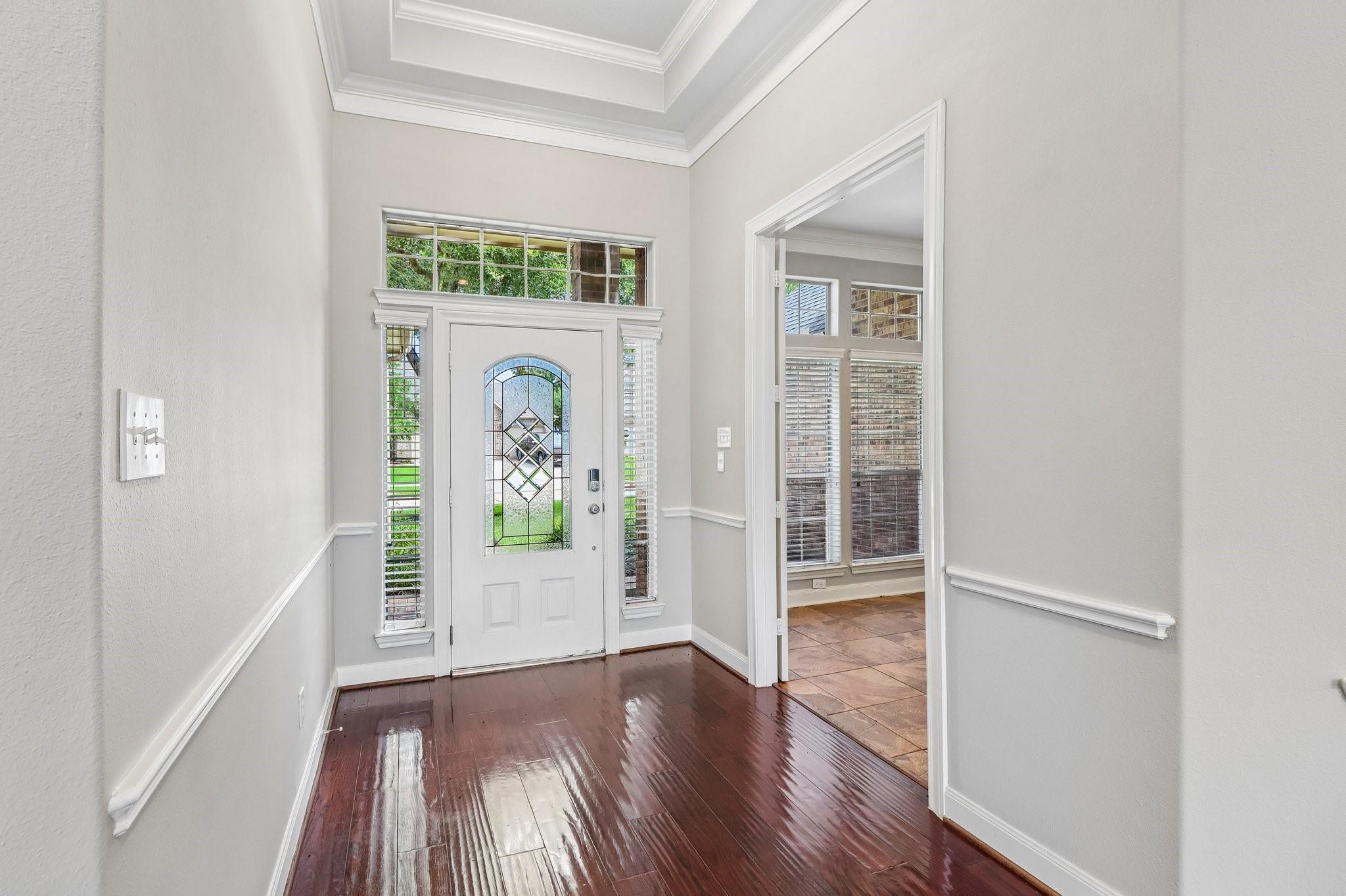 Entry foyer with glossy hardwood floors, a decorative glass front door, and an open doorway to a tiled room.