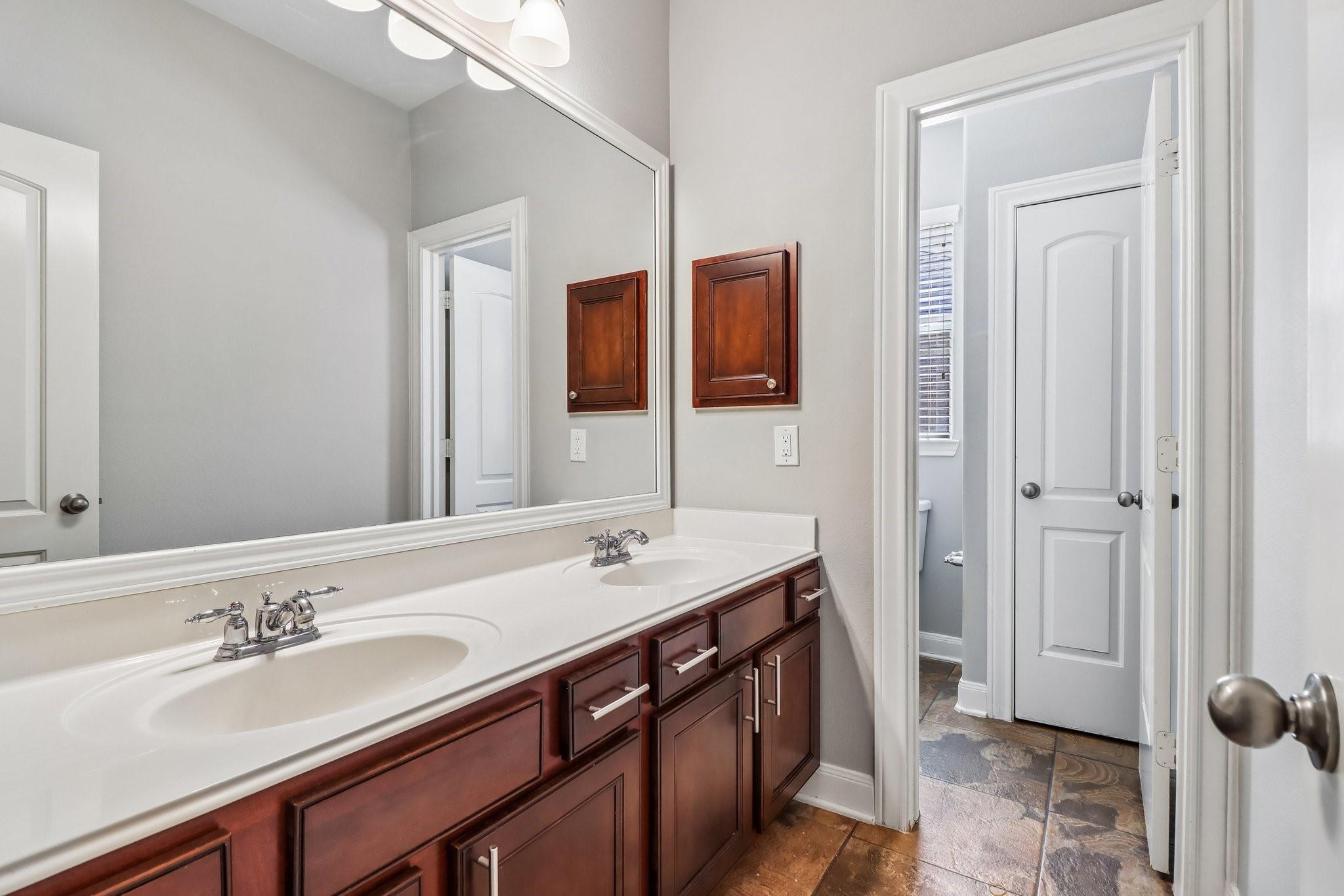 Bathroom vanity with two sinks, dark wood cabinets, a large mirror, and a doorway to the toilet area.