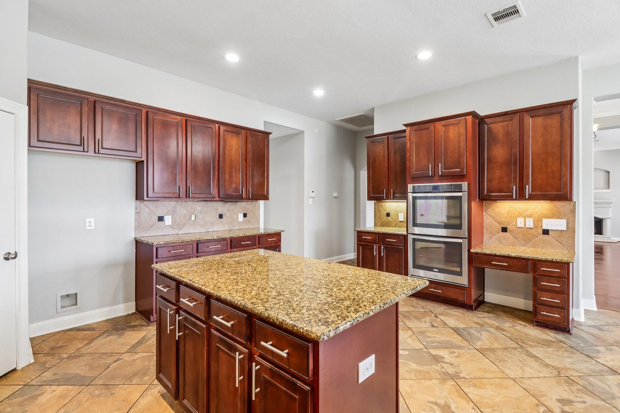Kitchen with a granite island, dark wood cabinetry, and double wall ovens.
