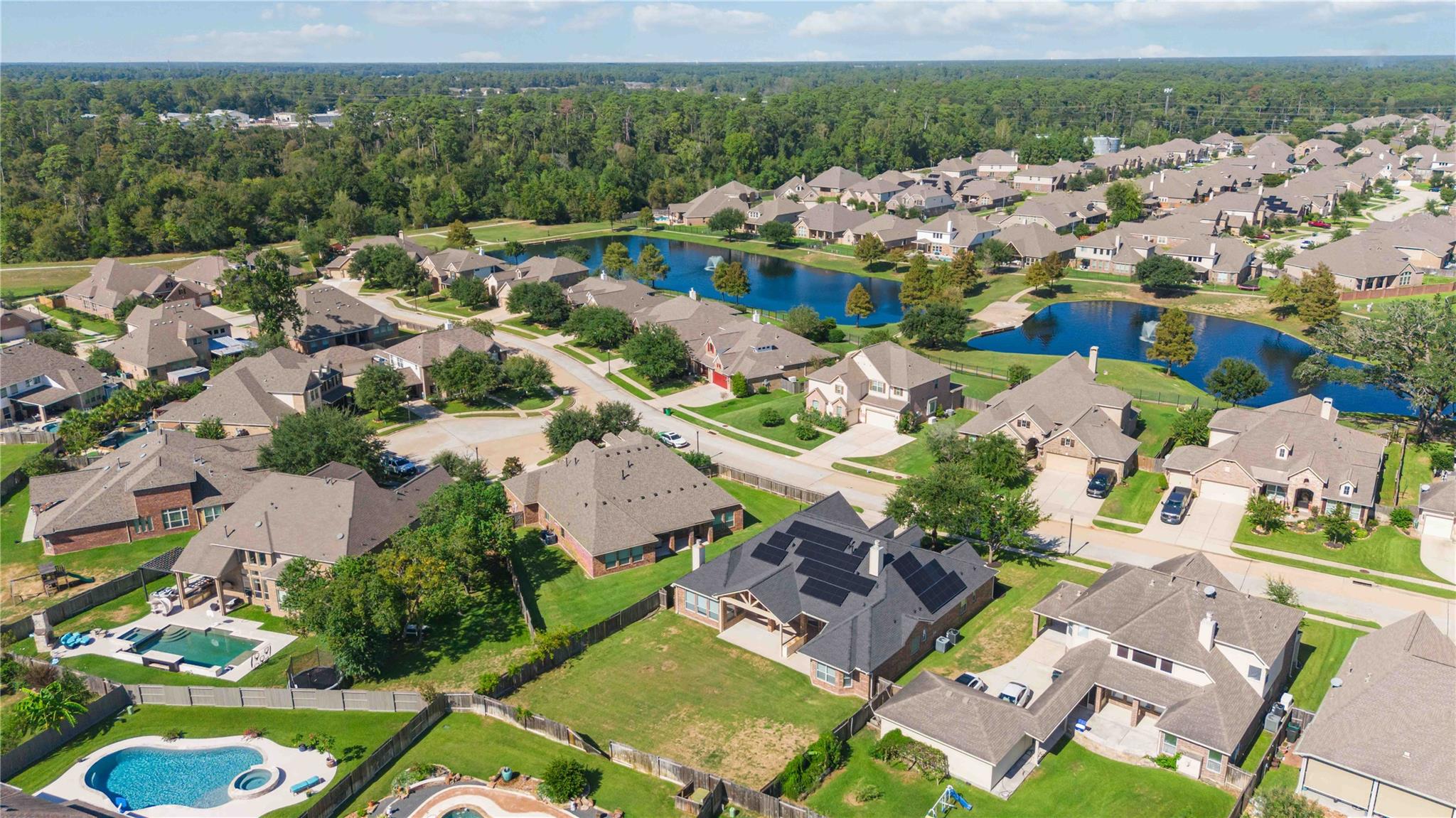 Aerial view of homes around two ponds with fountains, with a backyard pool in the foreground.