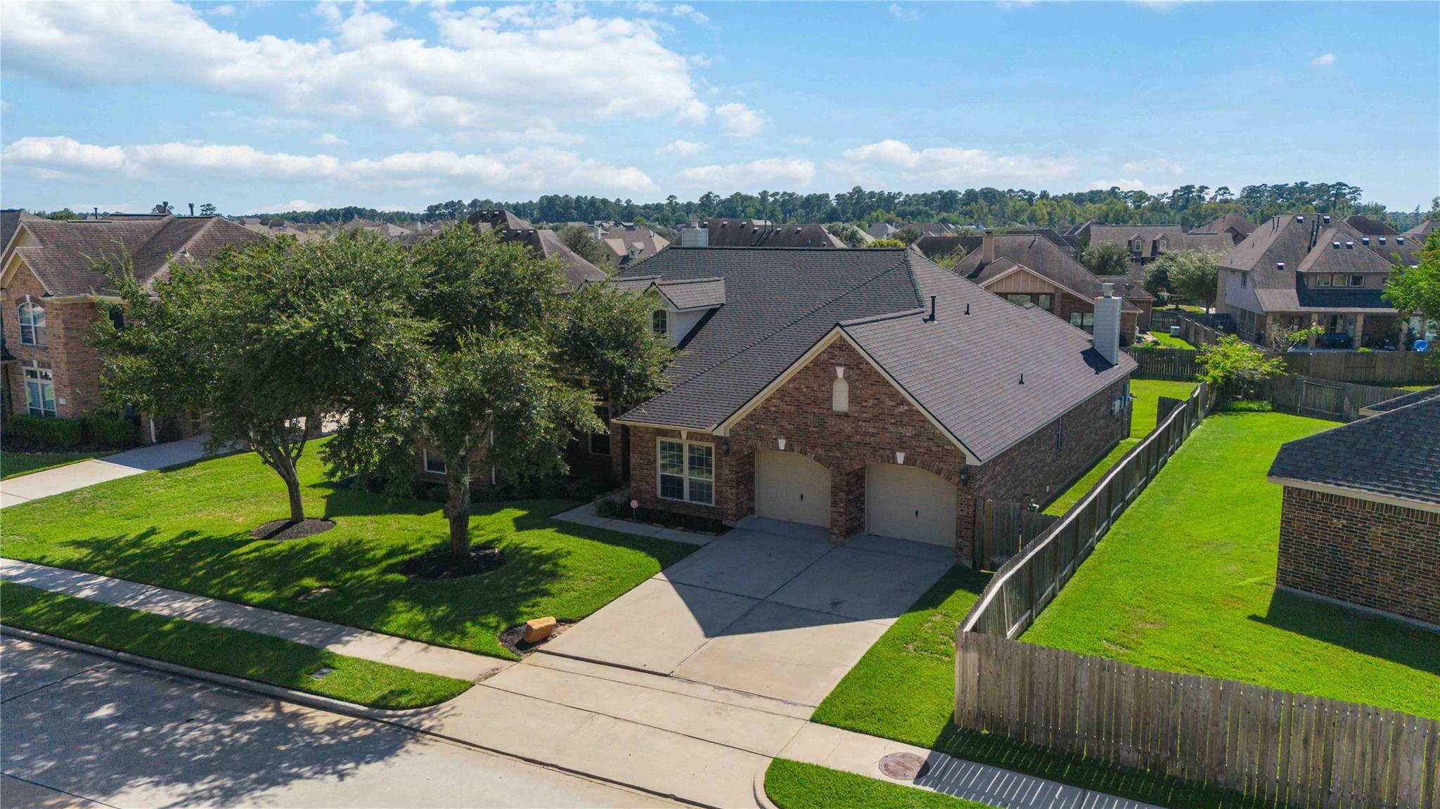 Aerial view of a brick home with a two-car garage, fenced lawn, and neighboring houses.