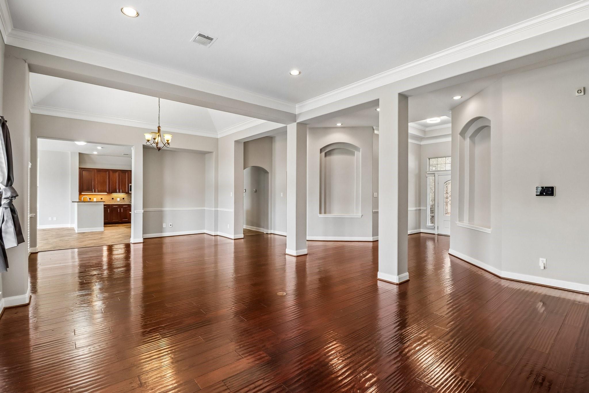 Vacant living and dining area with glossy hardwood floors, white columns, and arched openings.