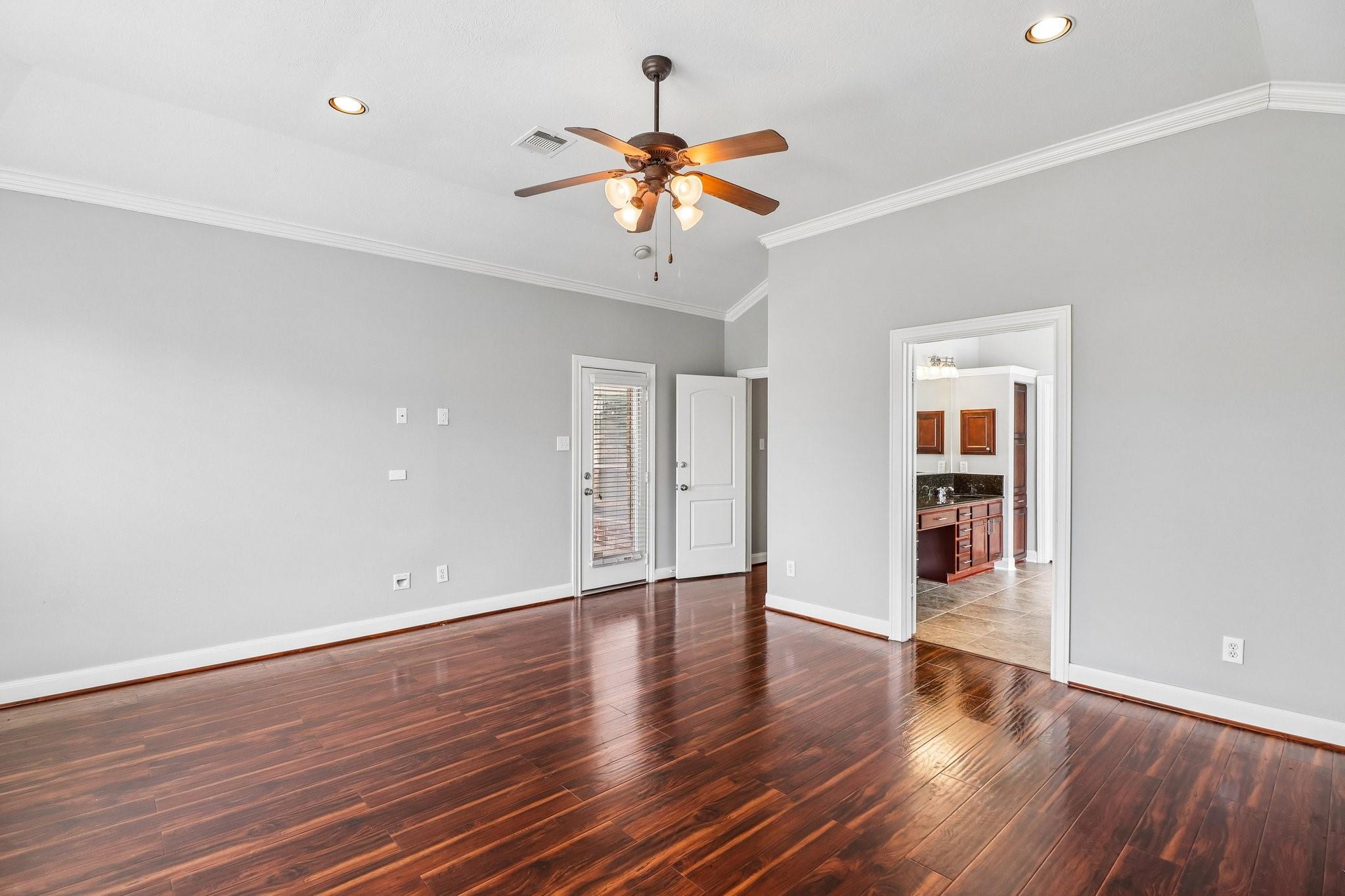 Empty room with dark hardwood floors and a ceiling fan, opening to a tiled vanity area.