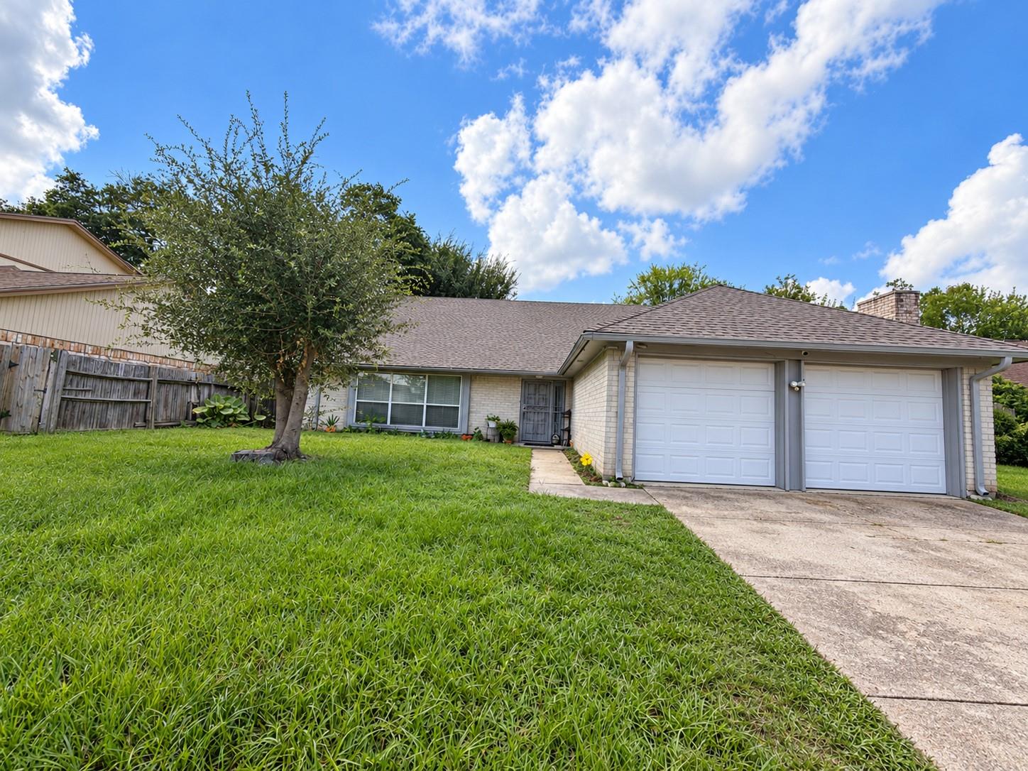 Single-story brick house with a two-car garage, broad lawn, and mature front-yard tree.