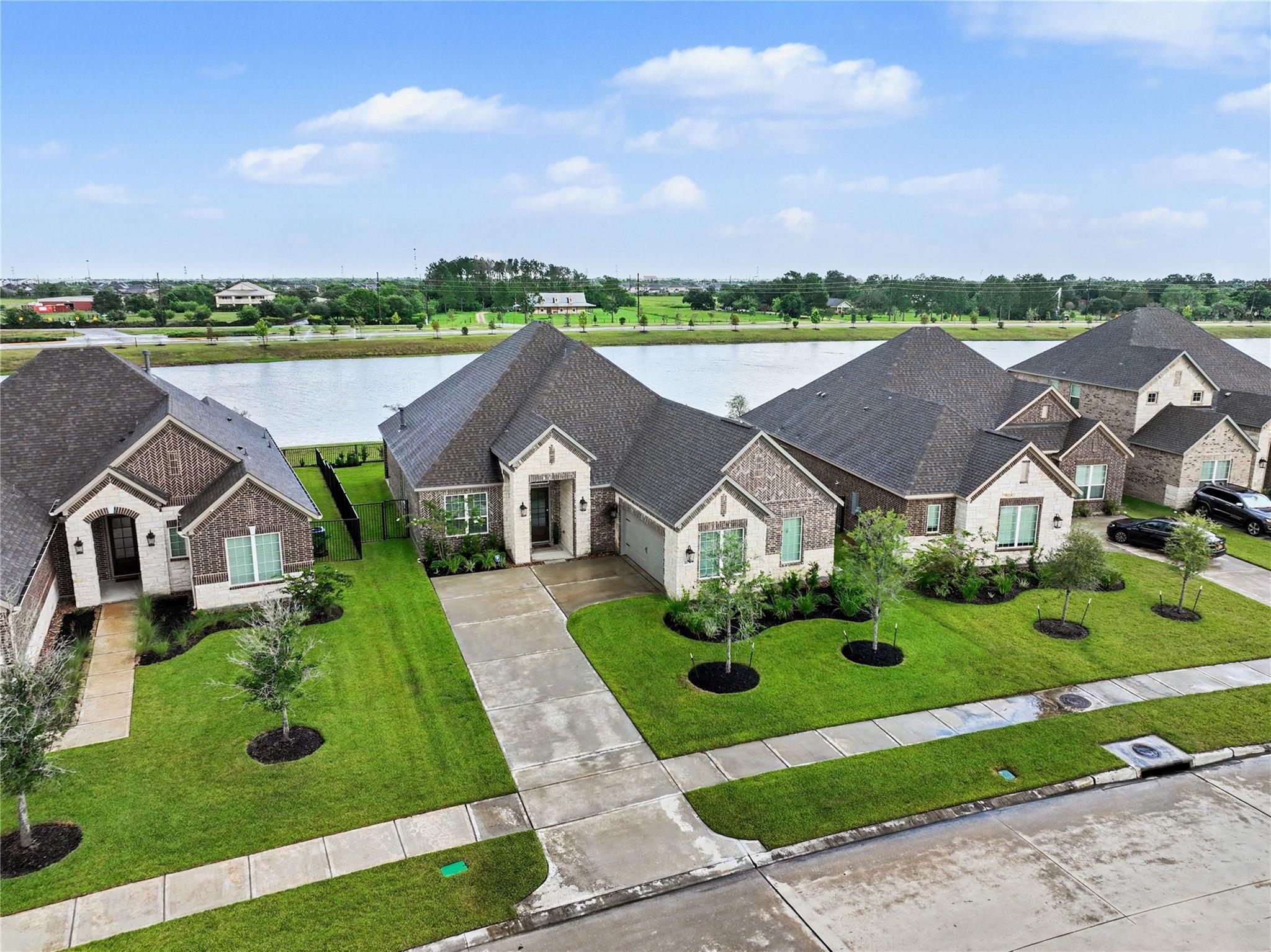 Aerial view of a brick home with a landscaped lawn beside a neighborhood lake.