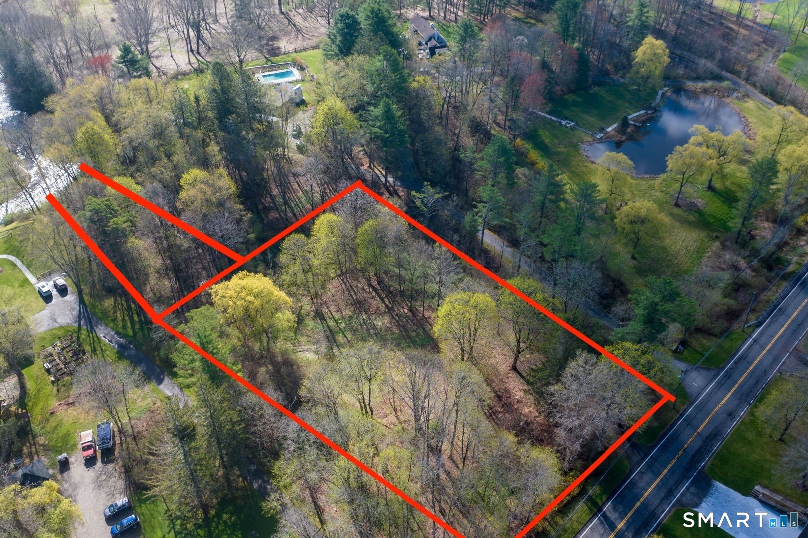 Aerial view of wooded land outlined in red beside a paved road.