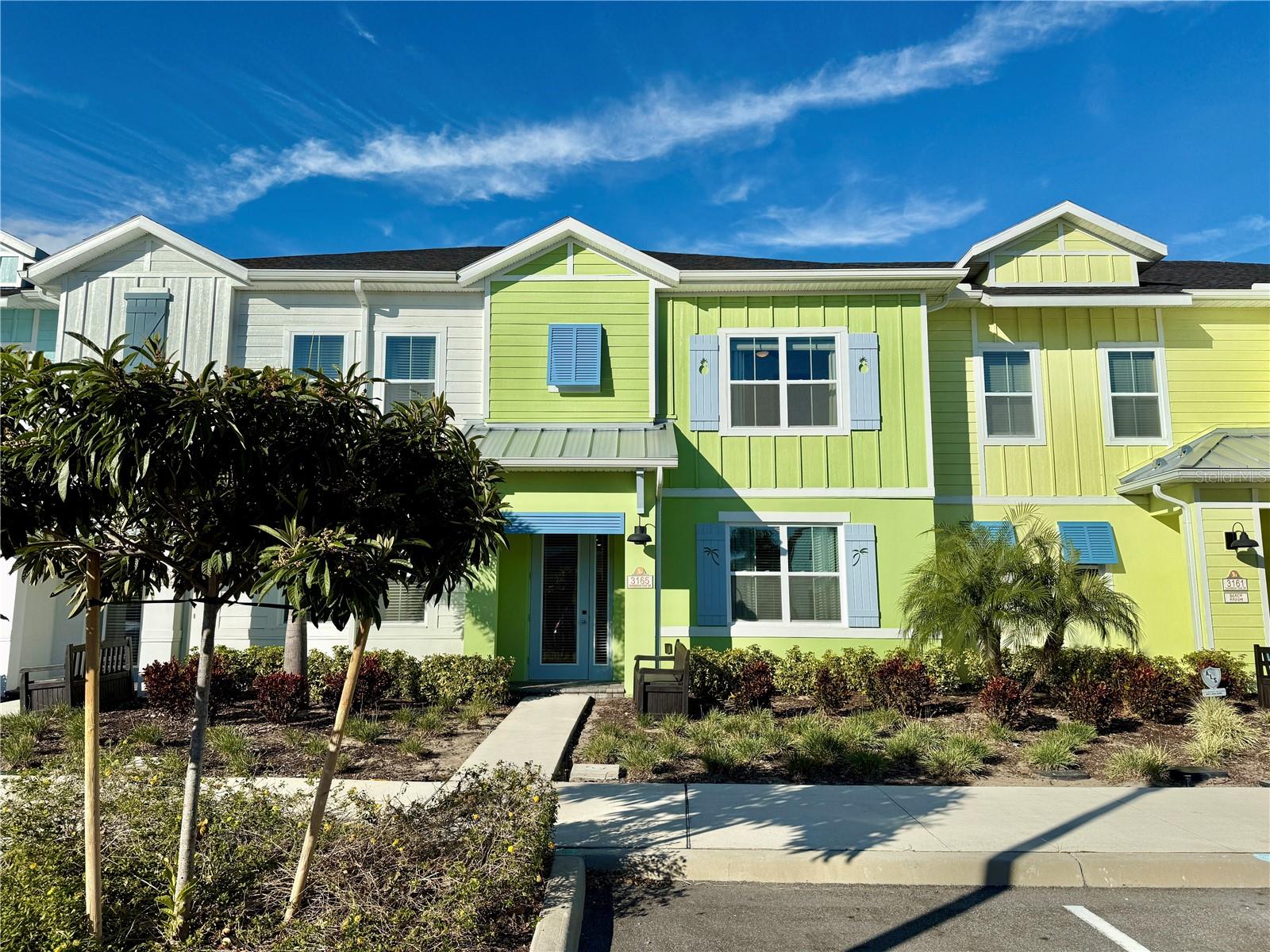Lime-green and white townhomes with blue shutters, landscaped frontage, and a walkway to the entrance.