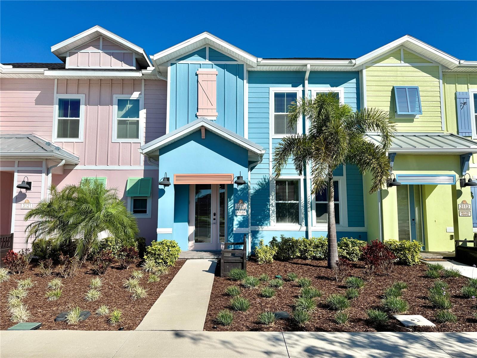 Colorful Margaritaville townhomes with a blue home centered between pink and lime-green facades and palm trees.