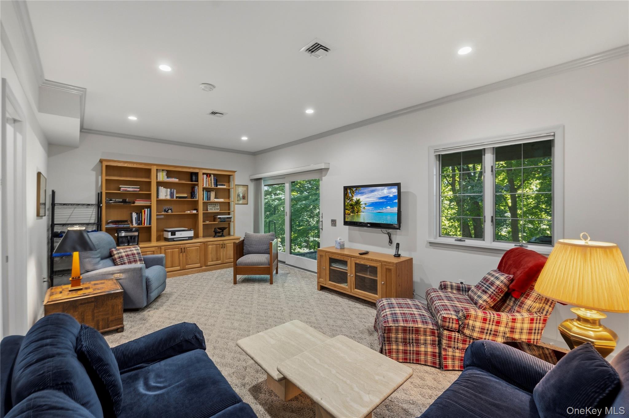 Living room with built-in wooden shelving, multiple seating areas, and windows overlooking trees.