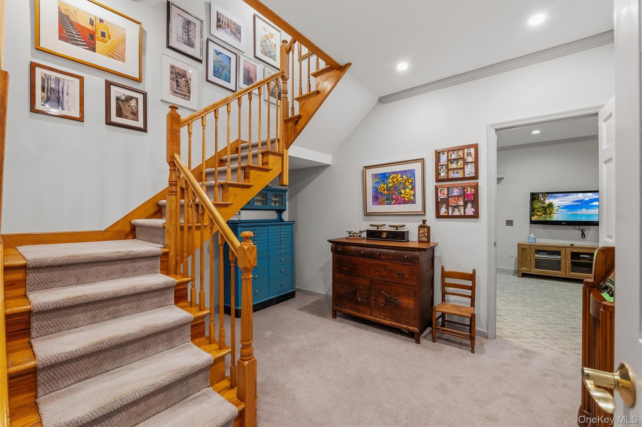 Carpeted staircase and furnished landing with wooden railings, framed art, and a blue cabinet beneath the stairs.