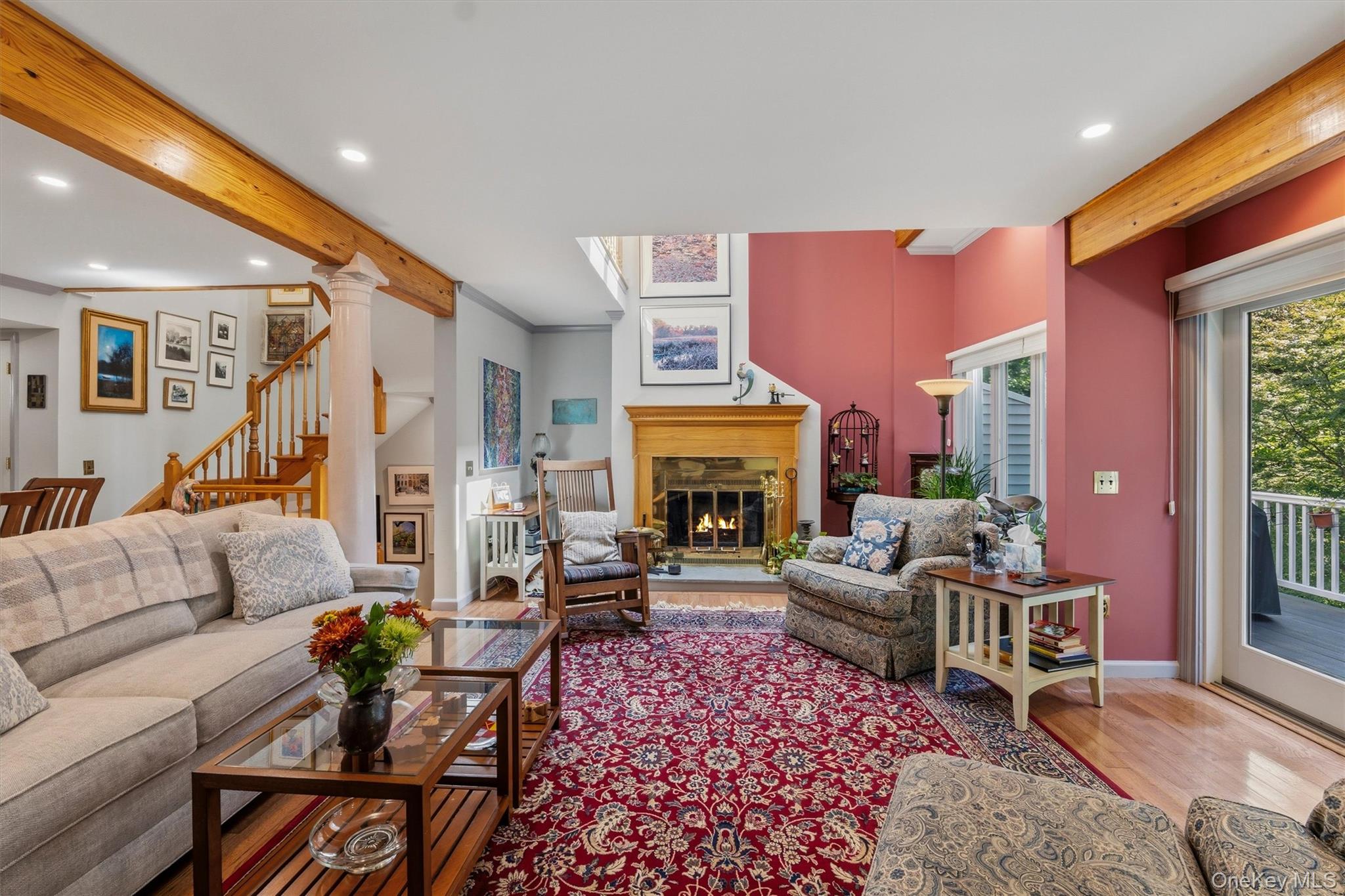 Living room with exposed wood beams, a fireplace, and glass doors to a deck.