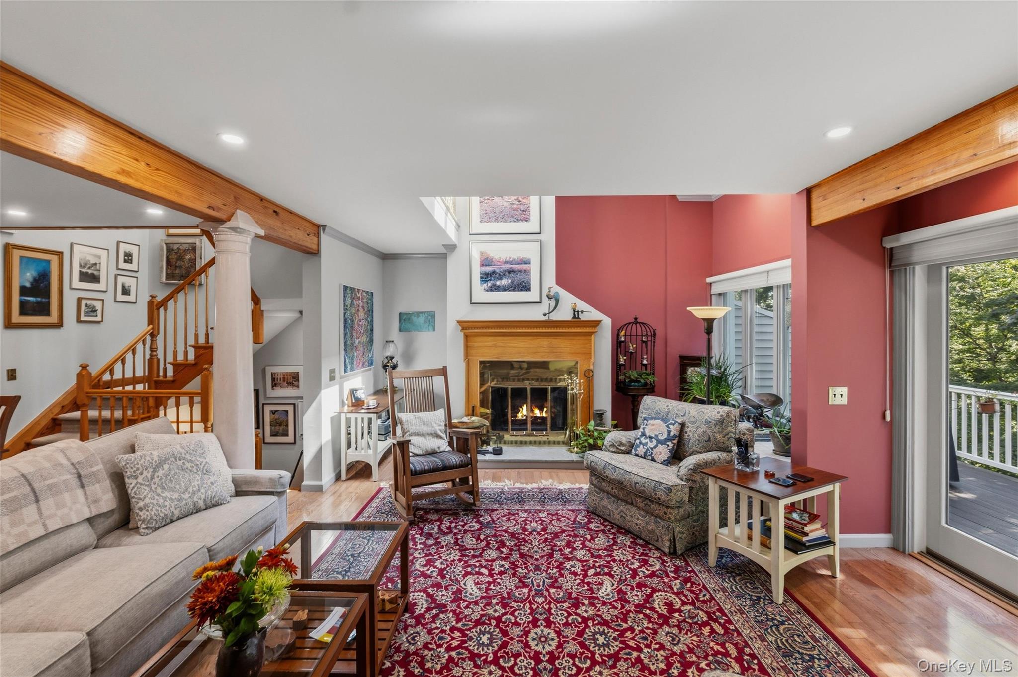 Living room with a wood-burning fireplace, exposed beams, and glass doors opening to a deck.