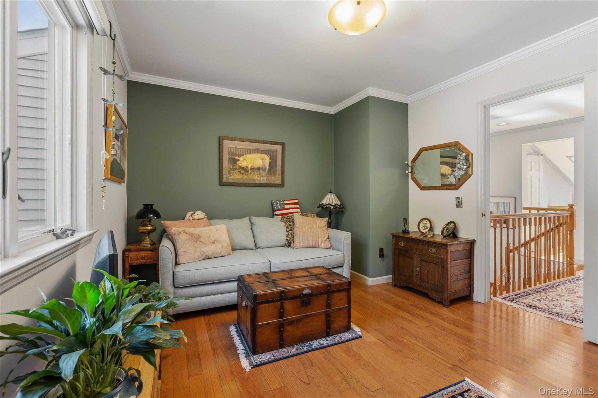 Living room with a gray sofa, green accent wall, wooden trunk coffee table, and hardwood floors.
